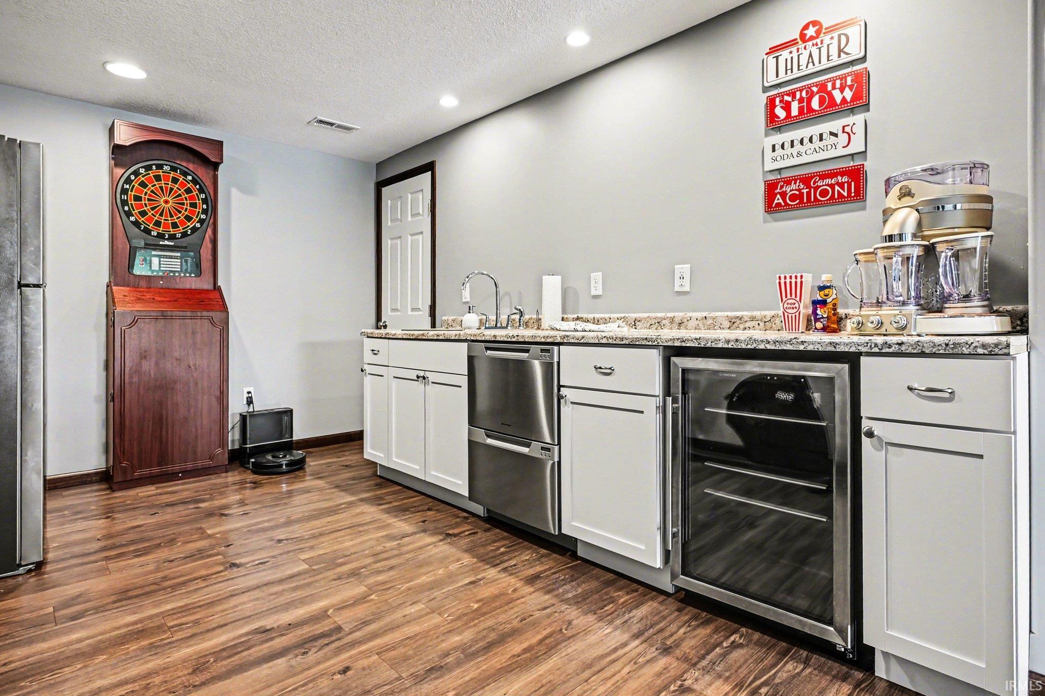 Wet bar featuring a stainless steel sink, wood-finish flooring, white cabinetry, a built-in beverage cooler, and granite-style countertops