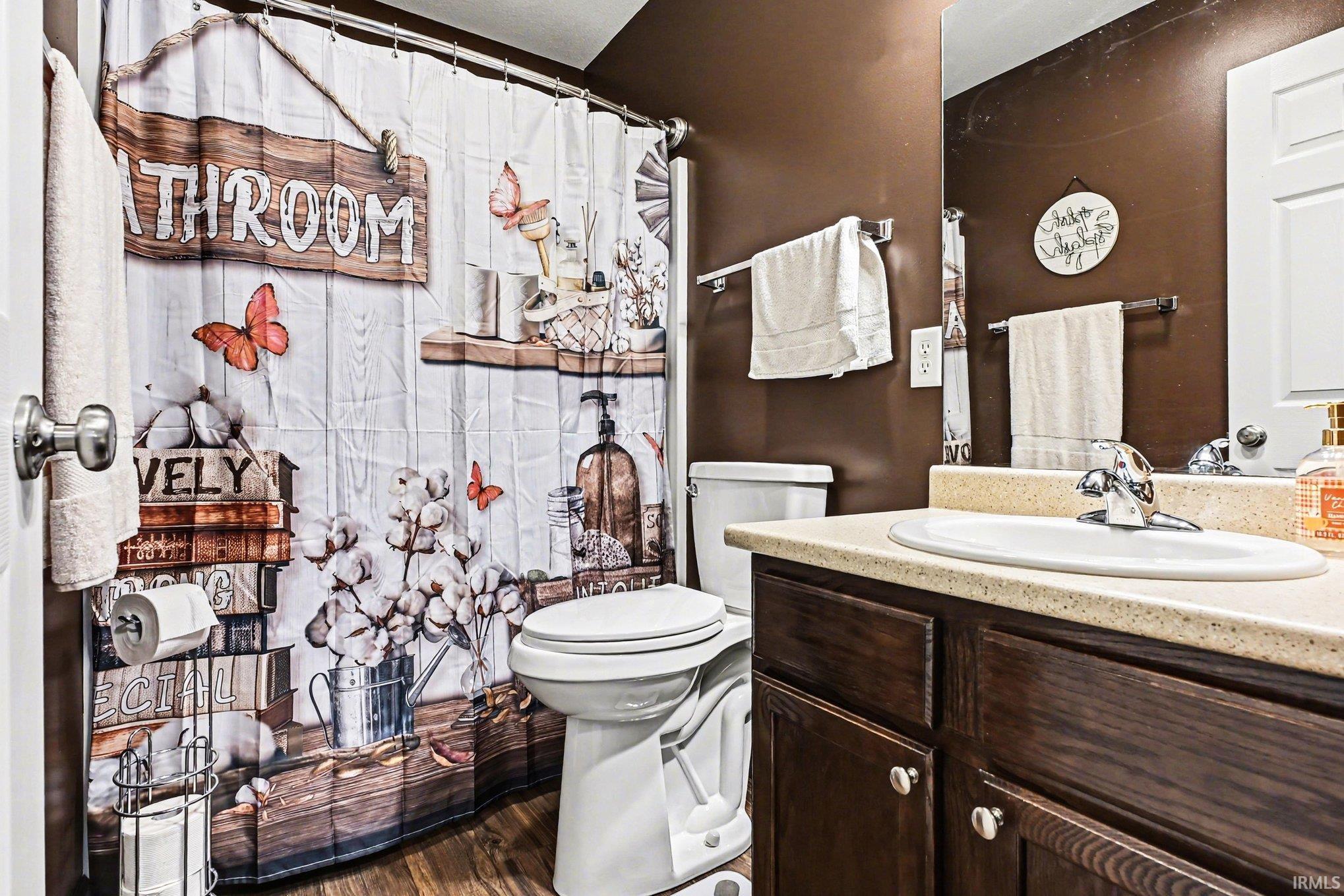 Bathroom featuring wood-finish flooring, a white toilet, and a vanity with a light-colored countertop and dark wood cabinetry