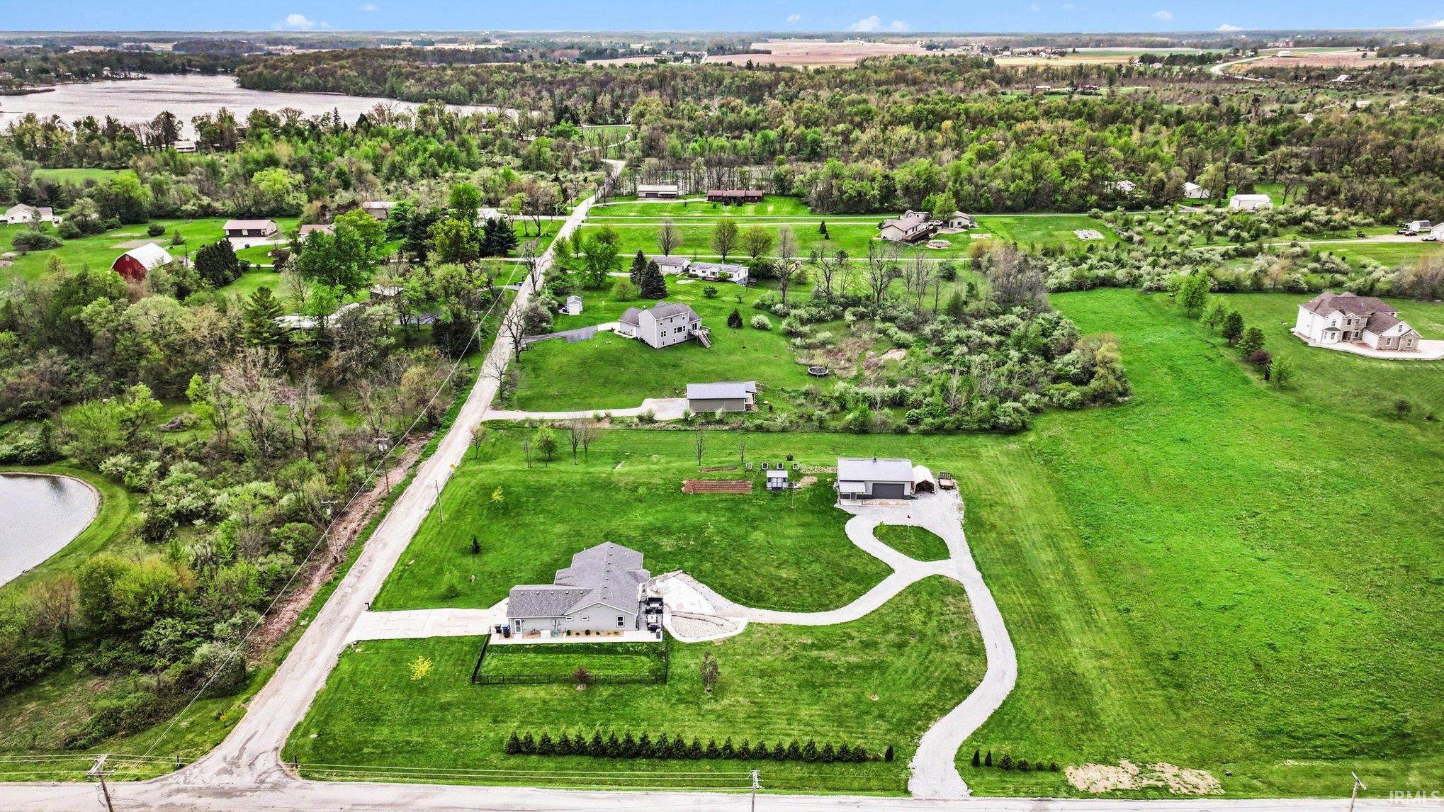 Aerial perspective showcasing a property featuring a light-colored exterior, a multi-car driveway, and a fenced yard with planted shrubs