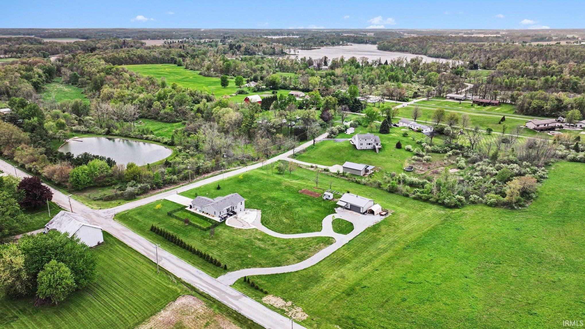 Expansive property featuring a paved driveway, manicured lawns, mature trees, and a visible body of water