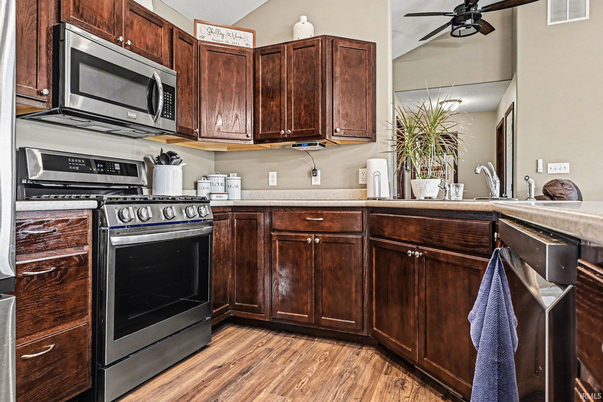 Kitchen featuring rich wood cabinetry, stainless steel appliances including a range and microwave, light-toned countertops, and wood-finish flooring