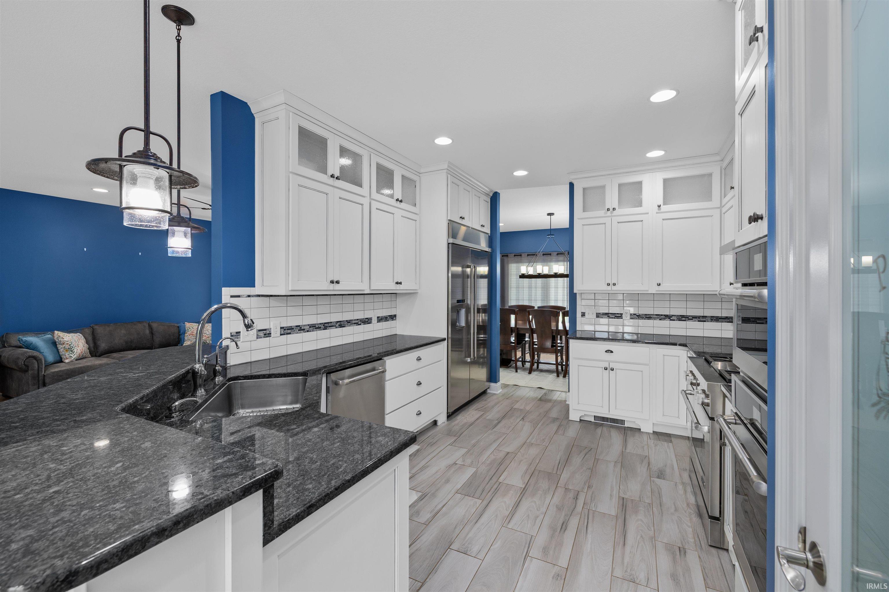 Kitchen featuring light wood-finish flooring, white cabinetry with glass-front accents, dark stone countertops, and a stainless steel sink with an extended faucet