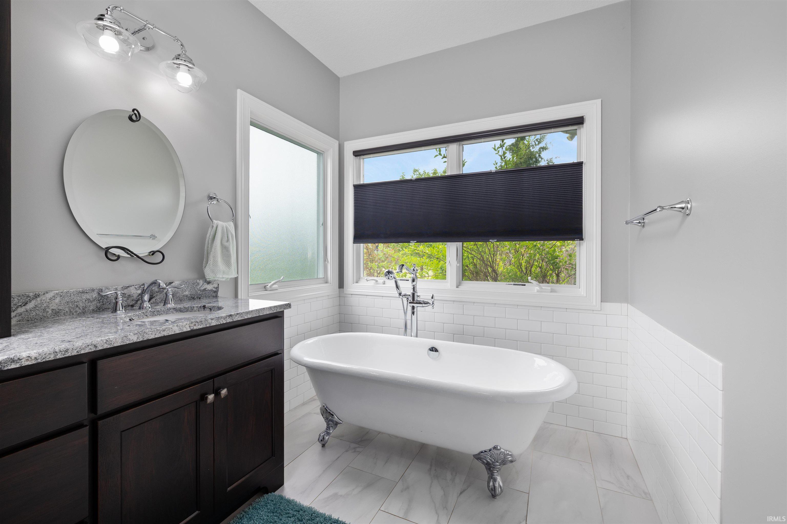 Clawfoot soaking tub with chrome fixtures, complemented by a dark wood vanity with a stone countertop and an oval mirror