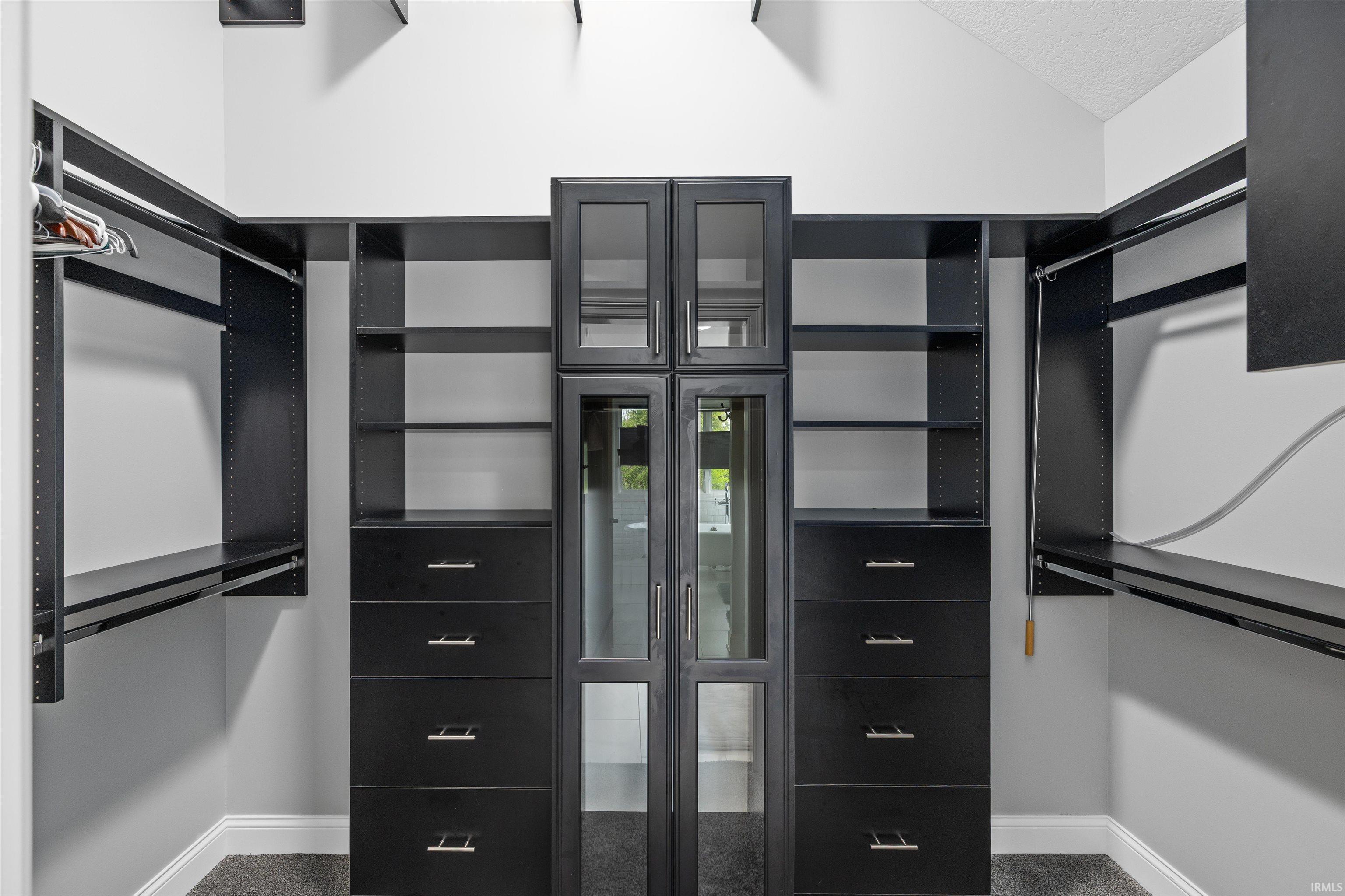 Custom closet system featuring dark wood-finish cabinetry, glass-front doors, multiple drawers with metal hardware, extensive shelving, and integrated hanging rods