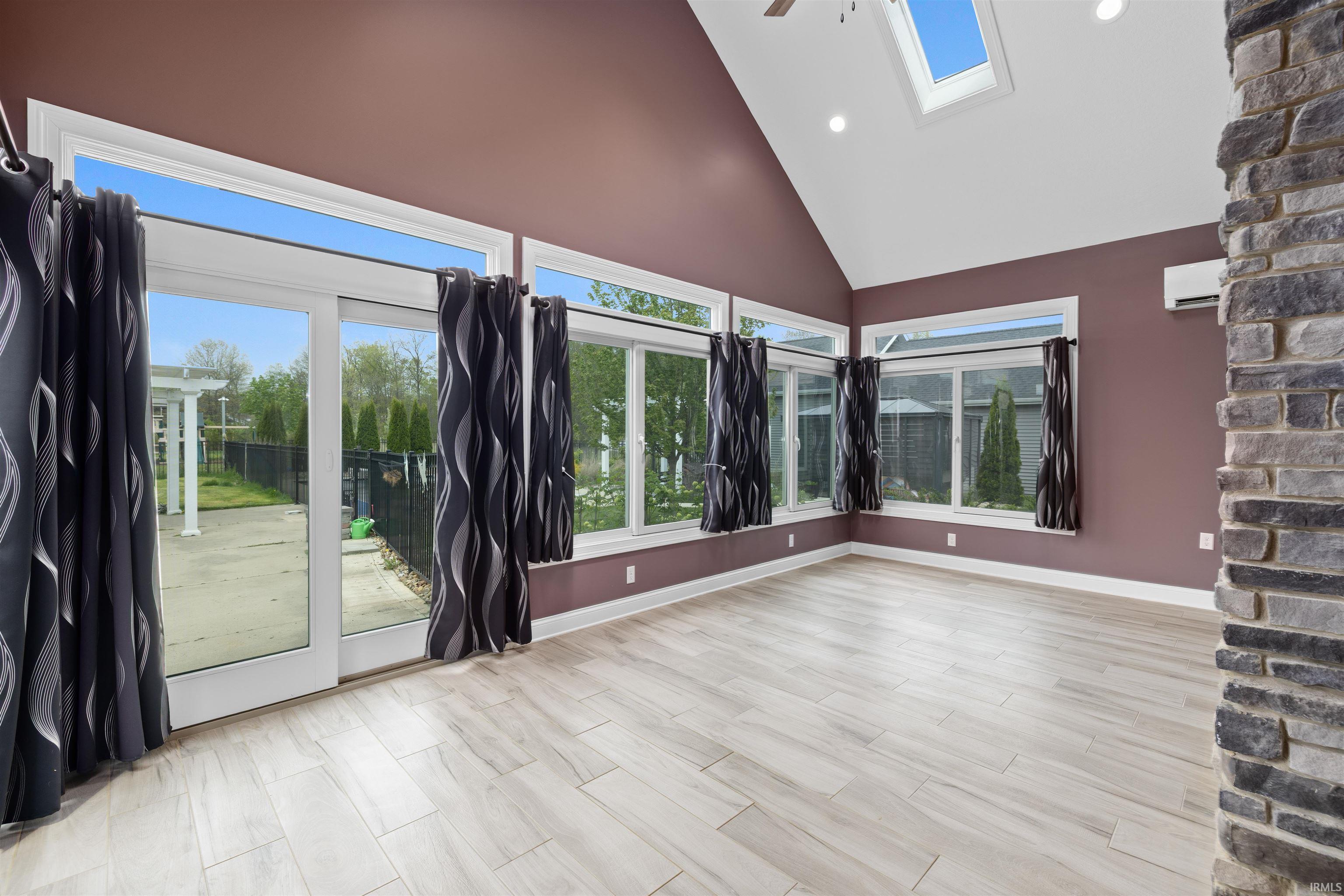Vaulted ceiling room featuring abundant windows, light wood-finish flooring, and a stone-clad architectural element