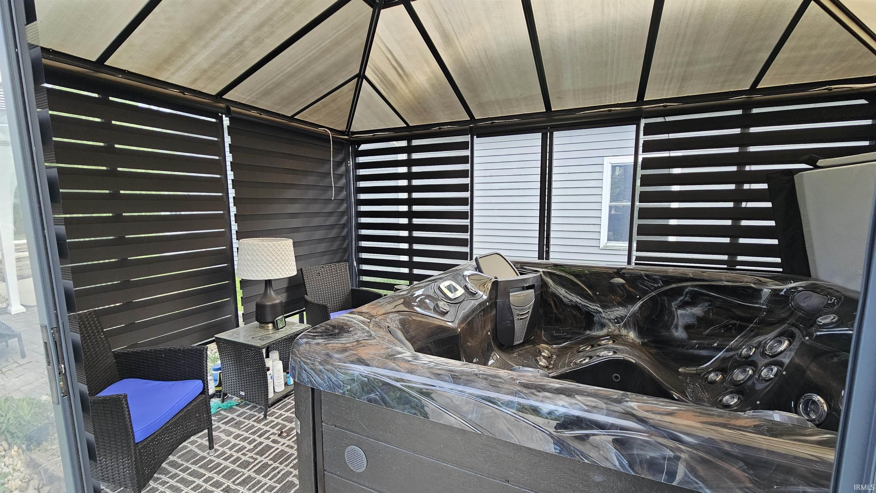 Covered outdoor spa enclosure featuring a black hot tub, fabric ceiling, slatted privacy blinds, and a textured area rug