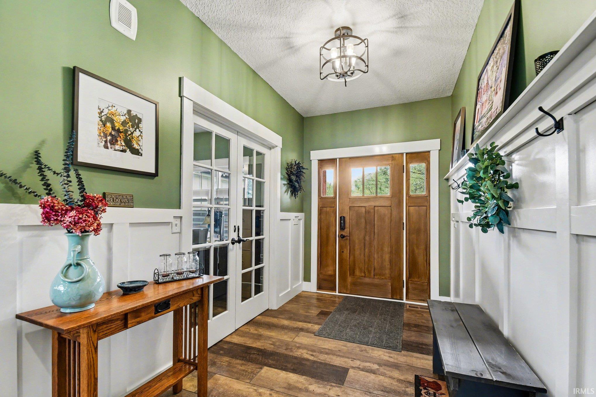 Entryway featuring a wood-panel front door with glass inserts, wood-finish flooring, white wainscoting, and French doors with glass panes