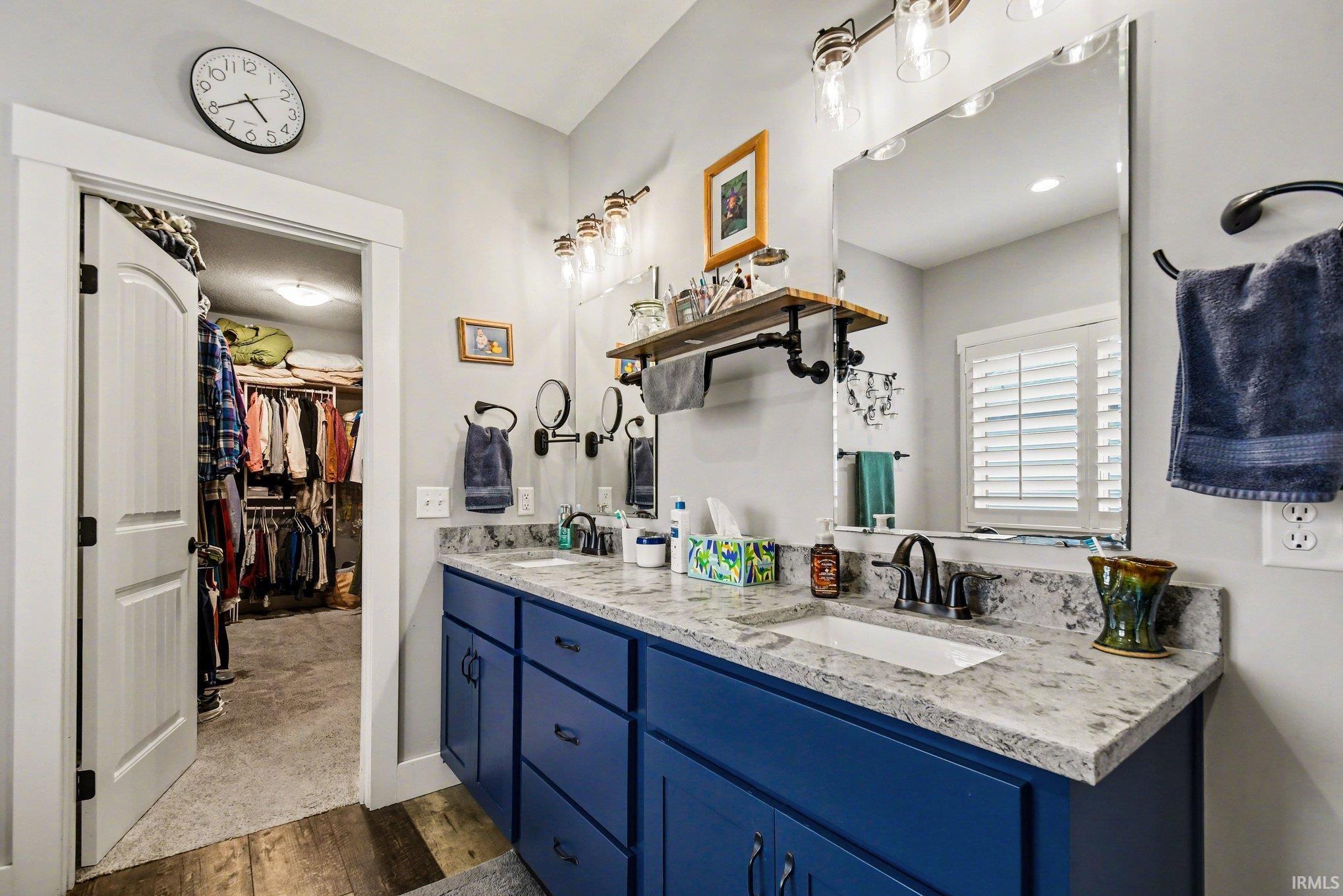 Bathroom vanity featuring dual sinks, blue cabinetry, and a light-toned stone-finish countertop