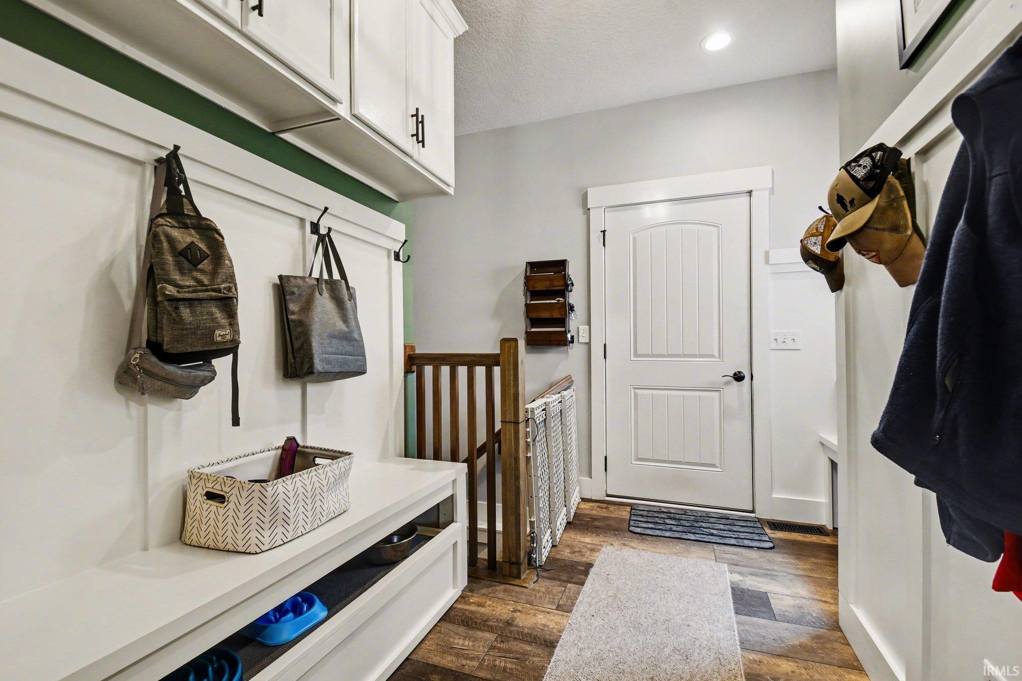 Entryway featuring wood-finish flooring, built-in bench seating, upper cabinetry with dark hardware, a panel-style door, and board and batten wall detailing