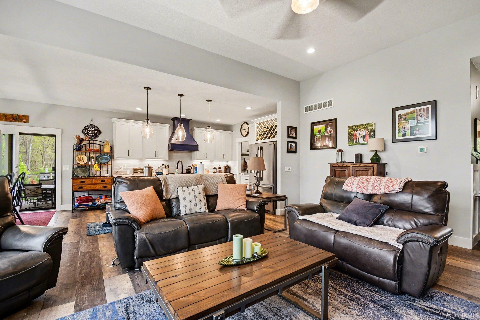 Spacious living area with wood-finish flooring and a ceiling fan, featuring an open concept layout into the kitchen