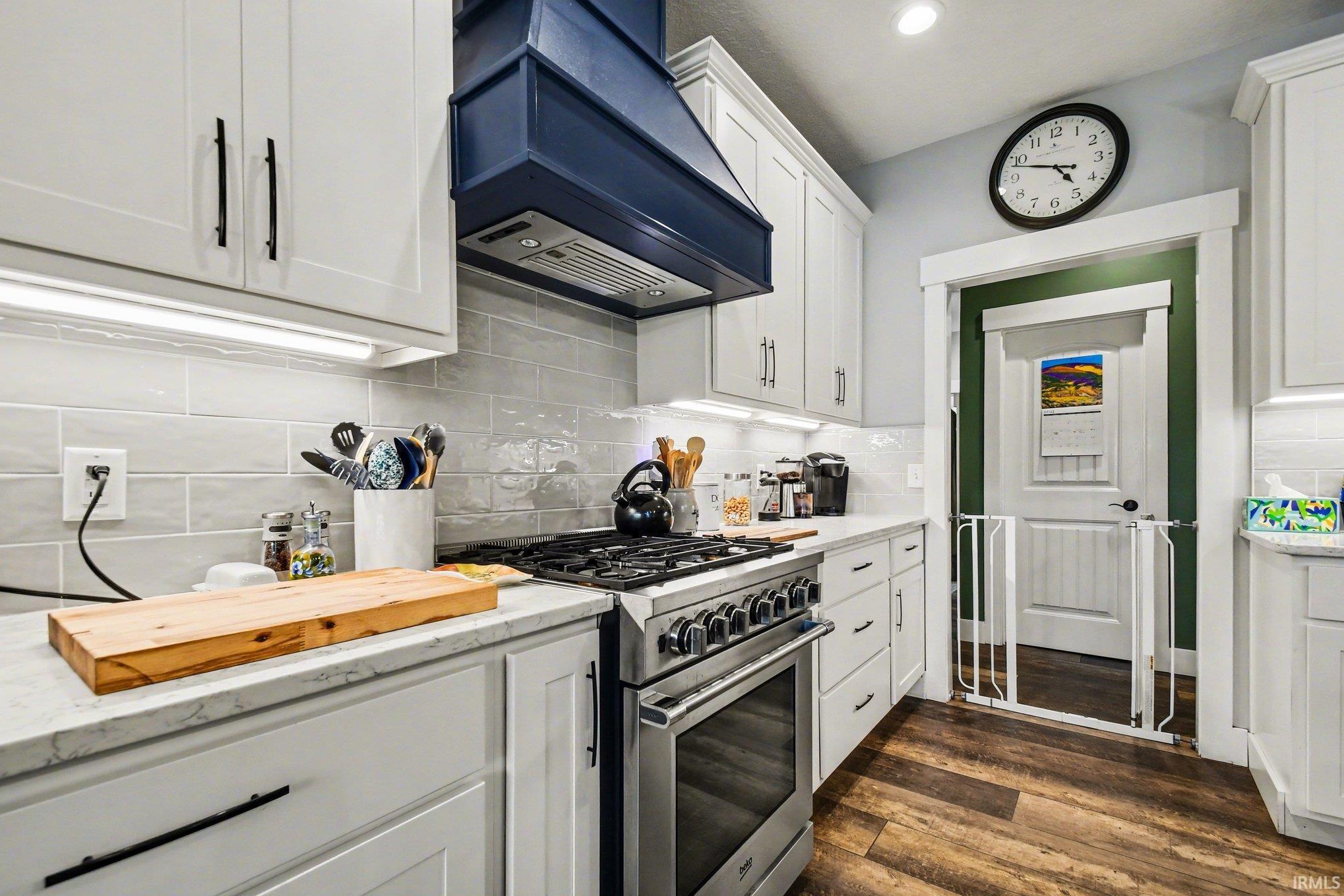 Modern kitchen featuring white shaker-style cabinetry with matte black hardware, light-toned subway tile backsplash, a stainless steel range, and a distinctive navy blue range hood