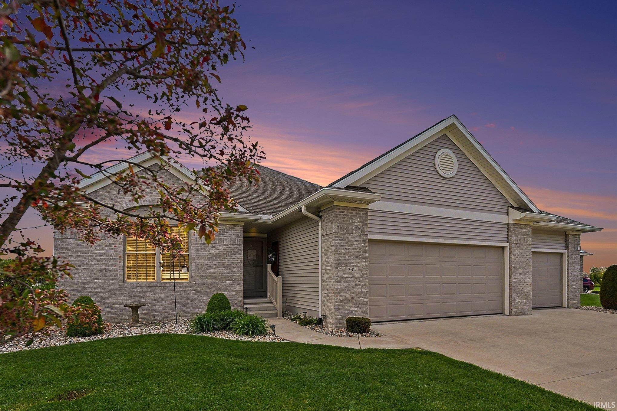 Brick and siding exterior featuring a multi-car garage, concrete driveway, and landscaped front yard with established shrubs