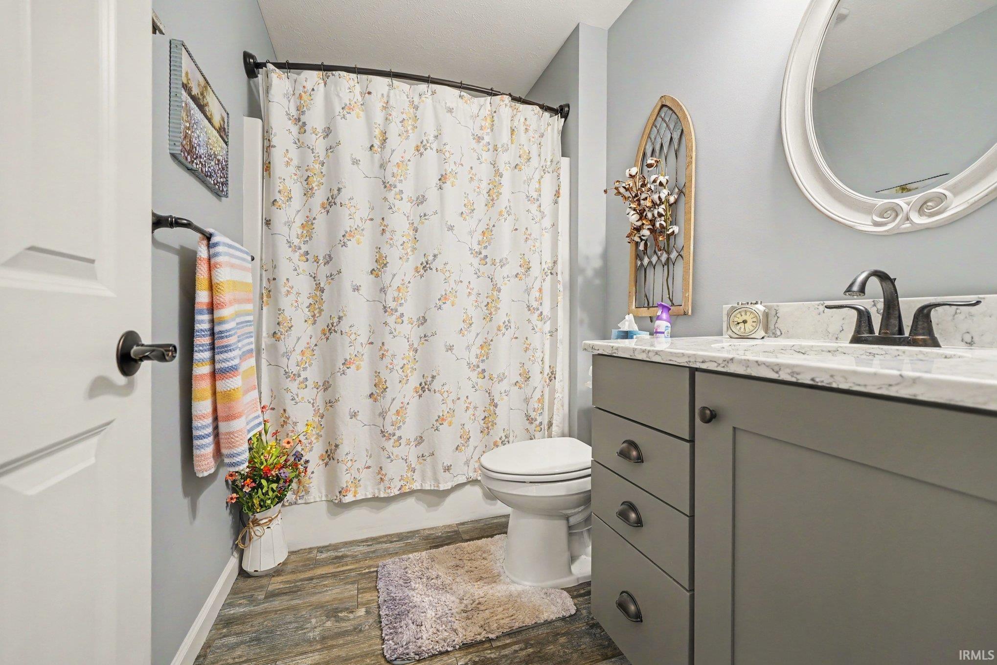 Bathroom featuring wood-finish flooring, a white vanity with a light-toned countertop, and a white oval-framed mirror