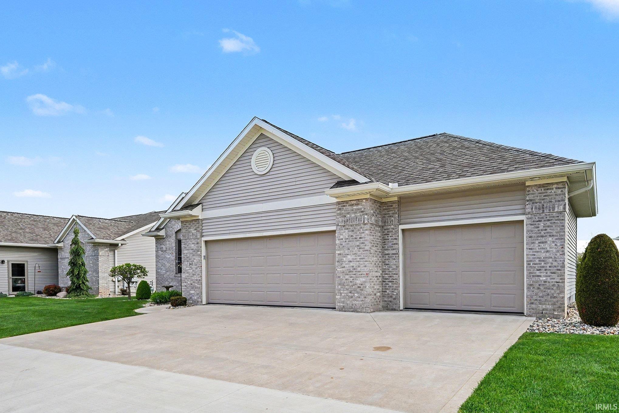 Exterior featuring a concrete driveway, two garage doors, light grey siding, and brick accents