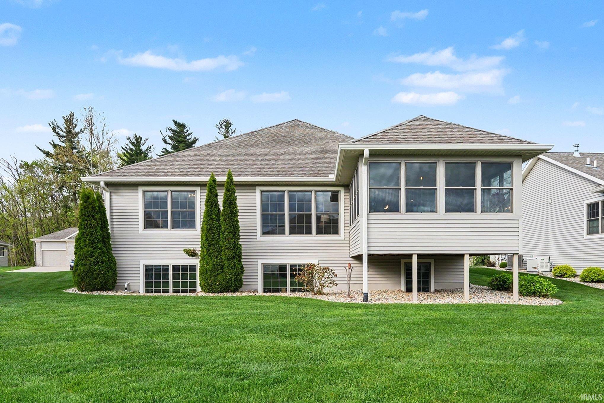 Rear exterior featuring light gray siding, a sunroom with multiple windows, a gabled roofline, and a spacious green lawn