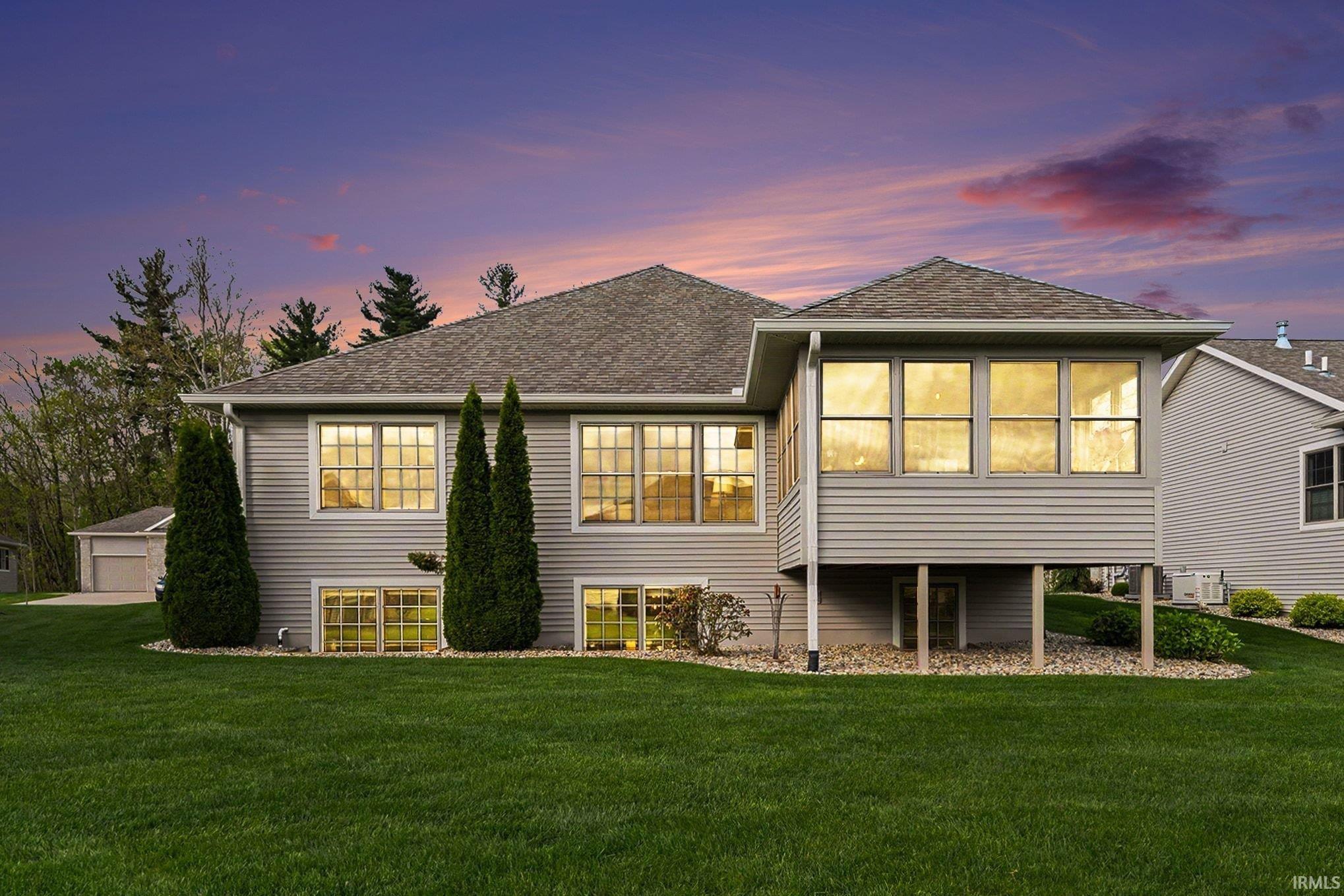 Spacious backyard featuring a manicured lawn, a multi-story home with light grey siding, multiple large windows, and a raised sunroom