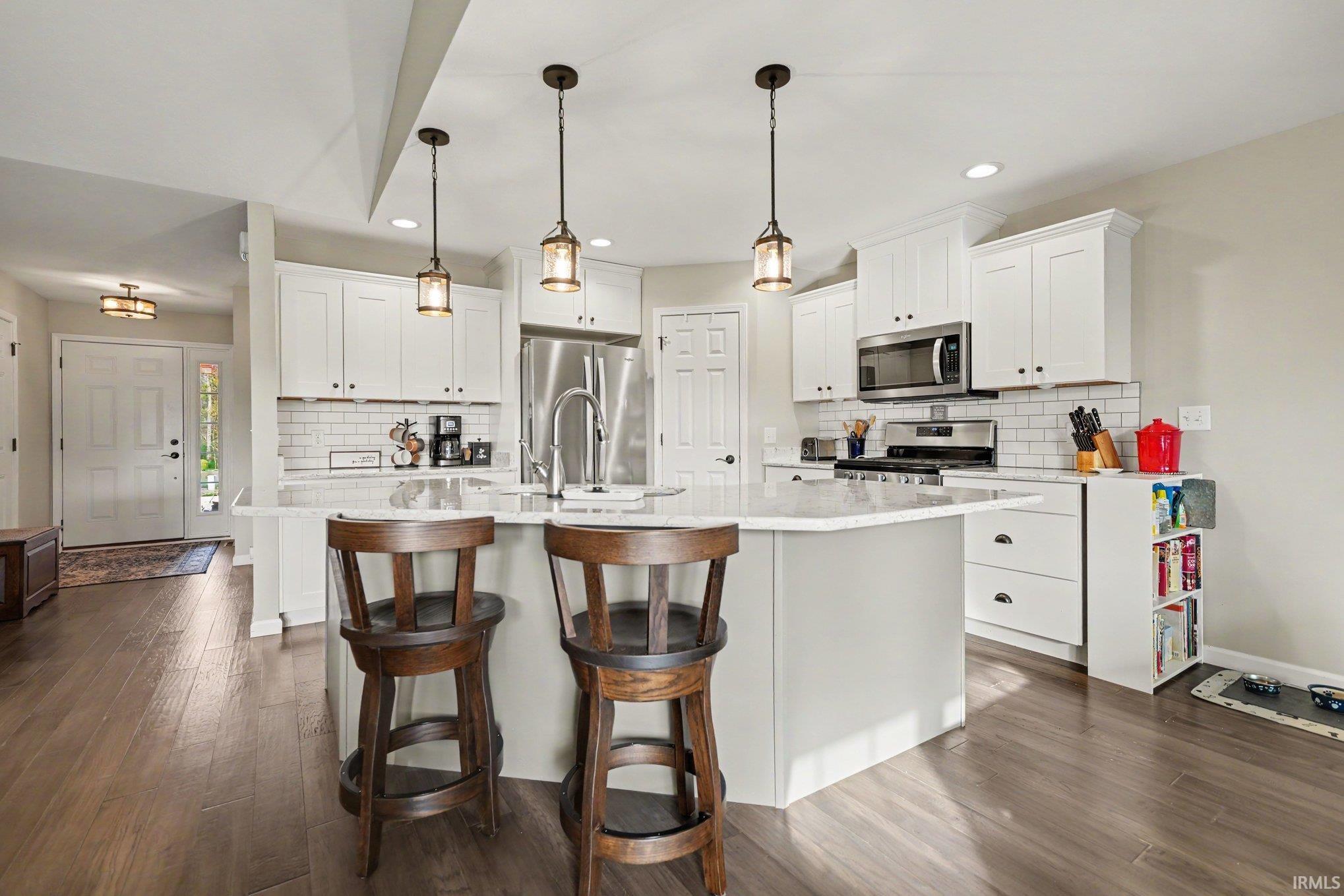 Modern kitchen featuring a central island with countertop seating, white shaker cabinetry, stainless steel appliances, and wood-finish flooring