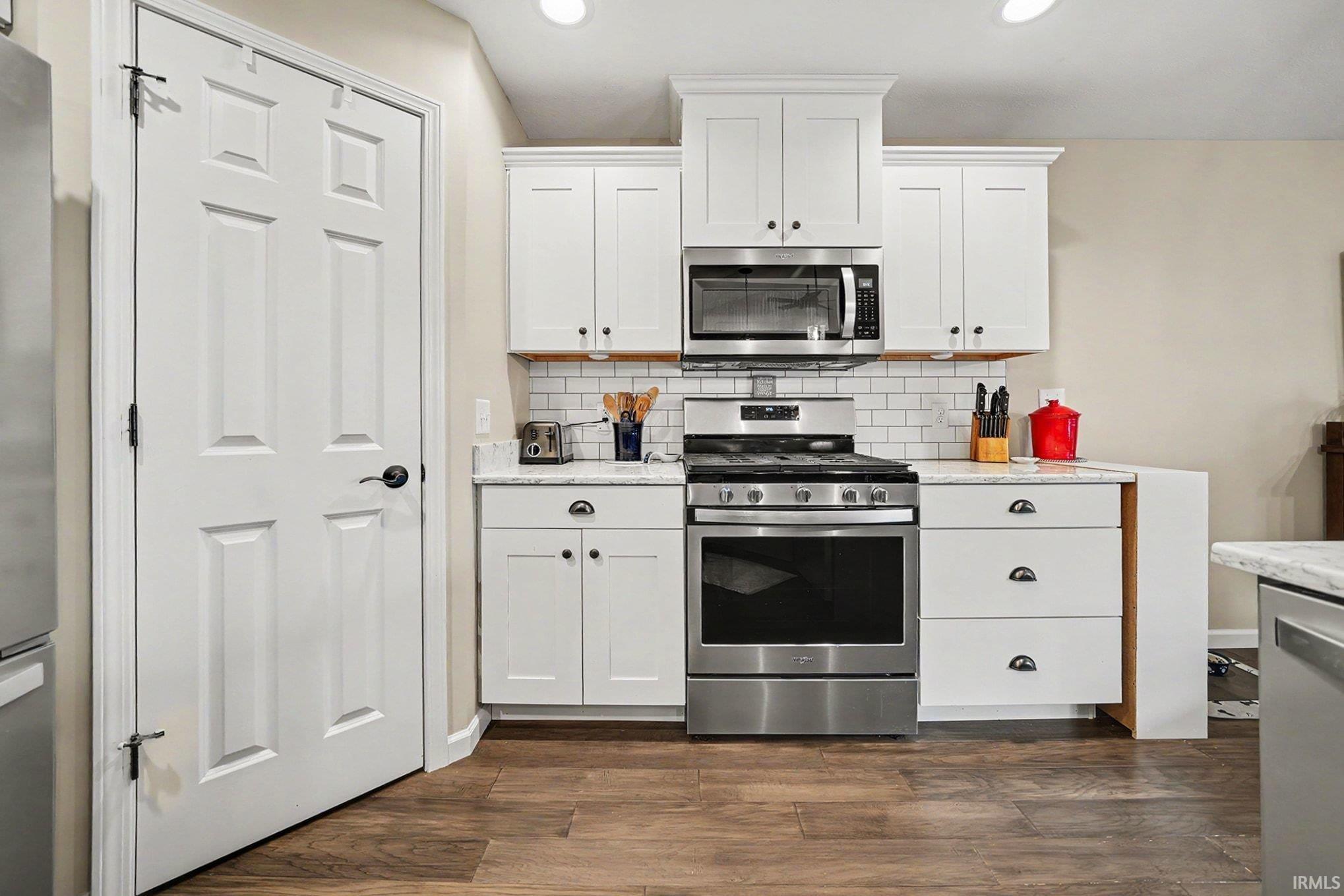 Kitchen featuring white cabinetry, stainless steel appliances, wood-finish flooring, subway tile backsplash, and recessed lighting