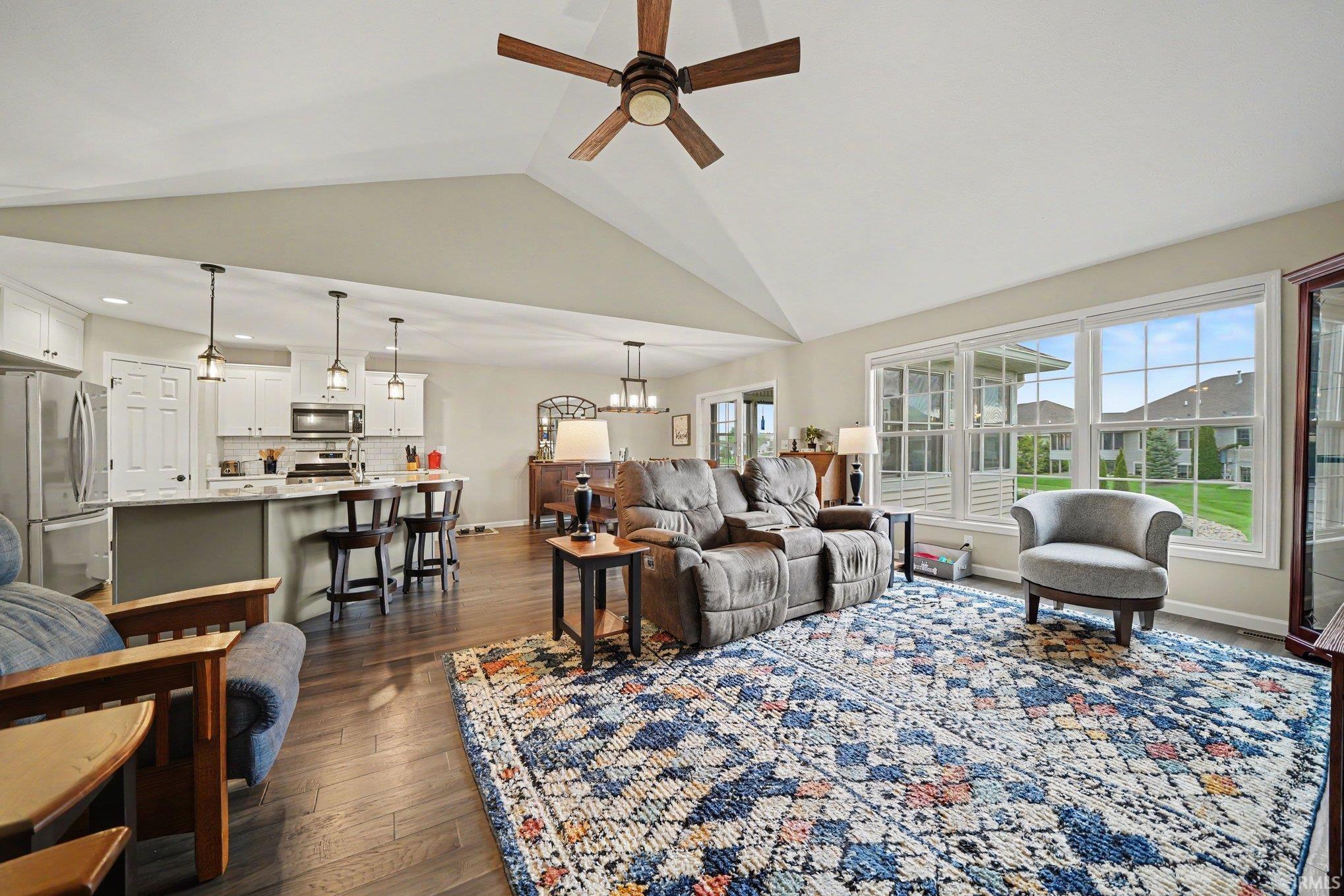 Open-concept living area featuring vaulted ceilings, wood-finish flooring, a ceiling fan, and multiple windows