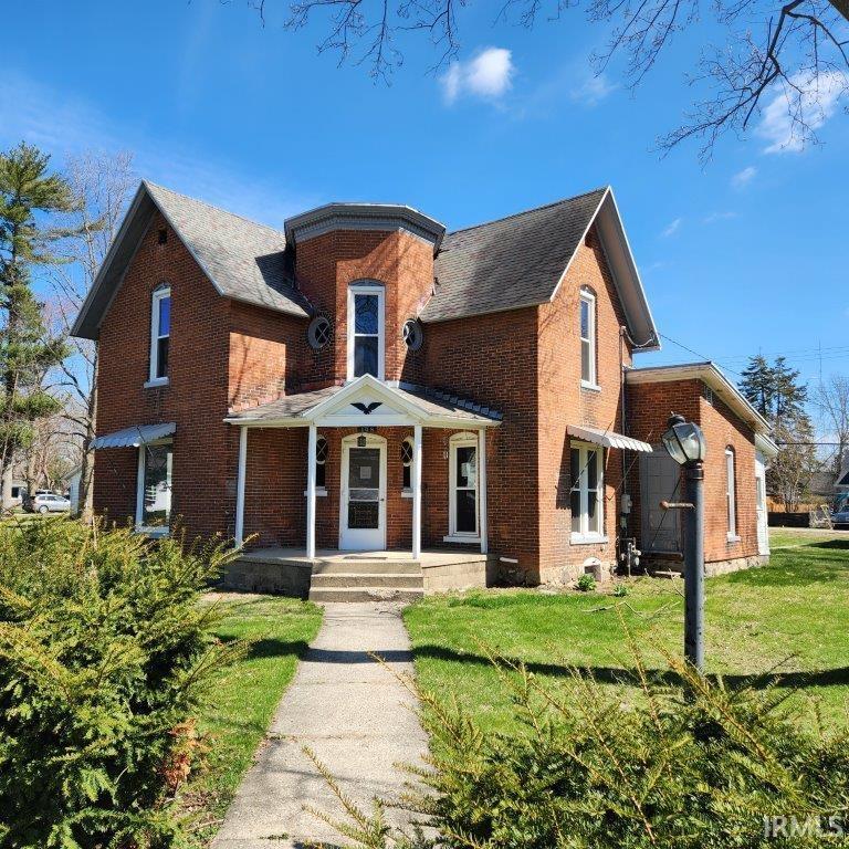 Brick facade residence featuring a covered front porch, an octagonal turret, multiple gabled rooflines, and a concrete walkway