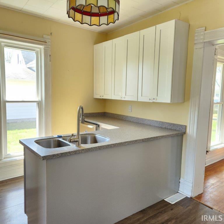 Kitchen area featuring a double basin stainless steel sink with a high-arc faucet, speckled countertops, and upper white shaker-style cabinetry