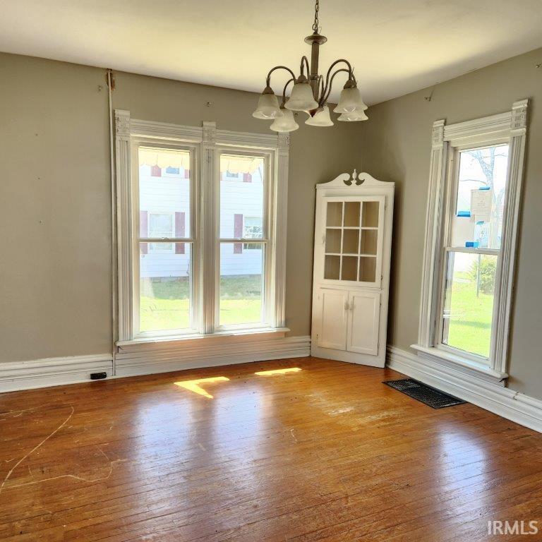 Hardwood flooring throughout featuring a corner built-in cabinet, ornate crown molding, and two large windows