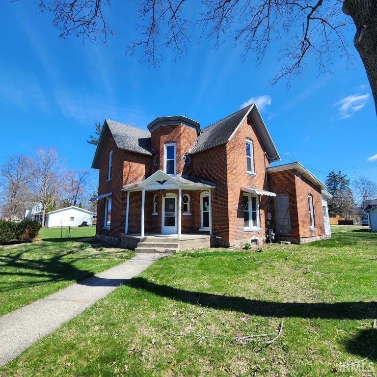 Brick exterior featuring a front porch with white columns, a turret with hexagonal roofing, a gabled roofline, and a concrete pathway