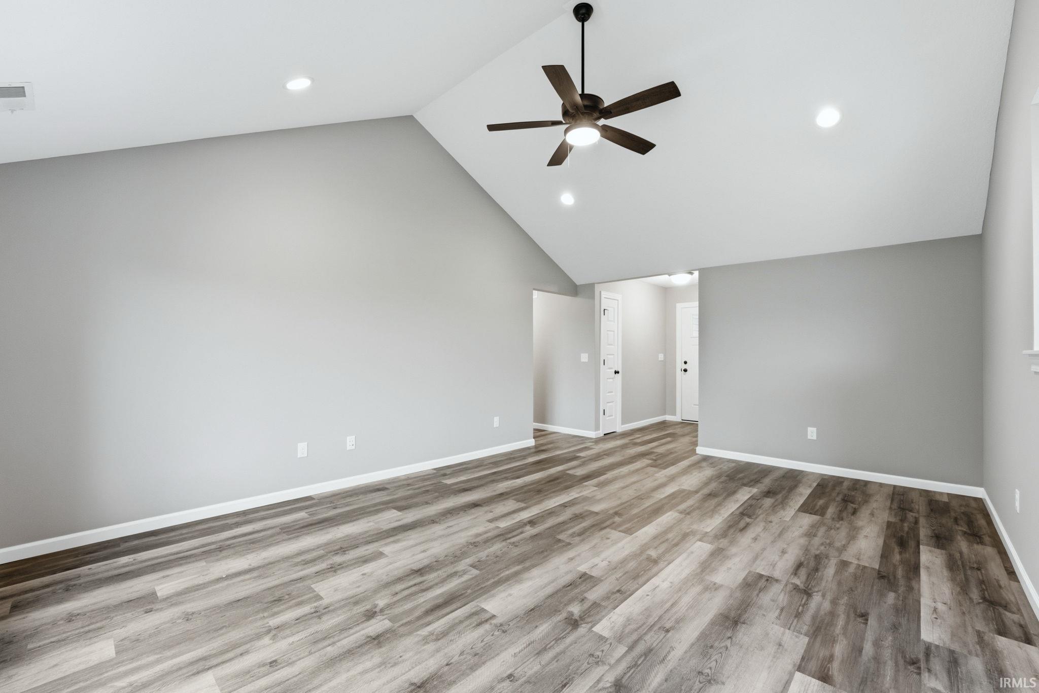Spacious room featuring vaulted ceilings, wood-finish flooring, a ceiling fan with integrated lighting, and recessed lighting