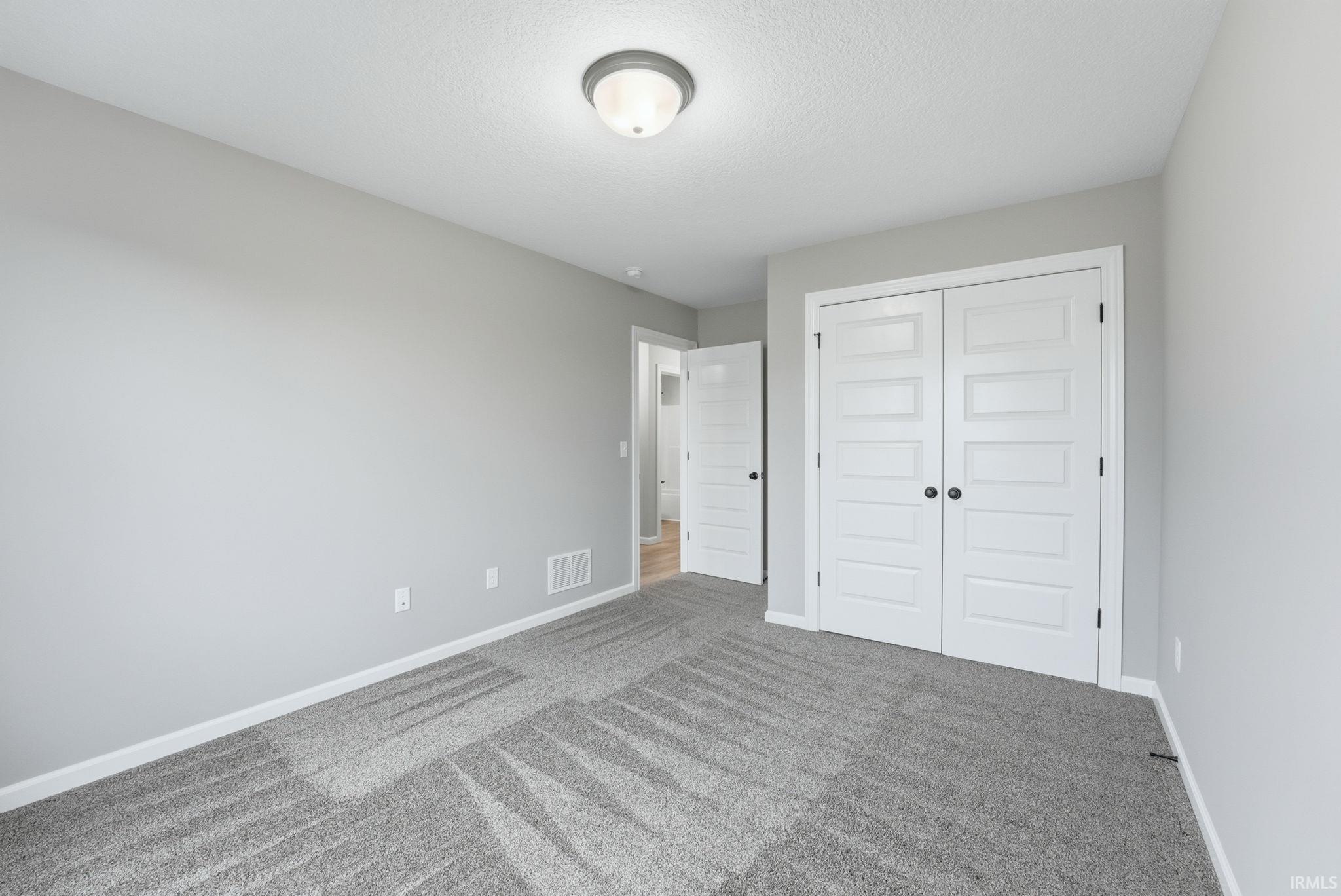 Bedroom featuring grey carpet with a geometric pattern, neutral wall paint, and white trim