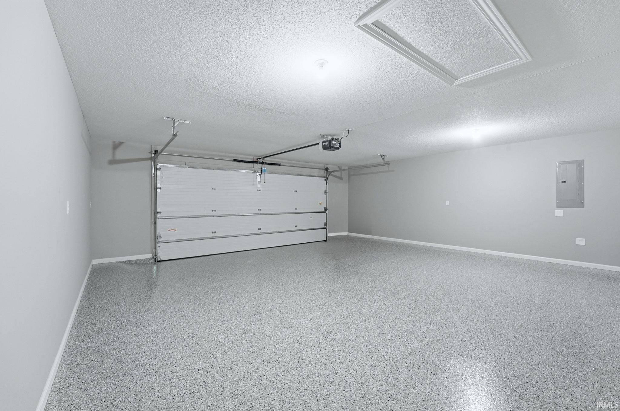 Spacious garage featuring a durable epoxy-coated floor, painted walls, automatic garage door opener, and overhead lighting