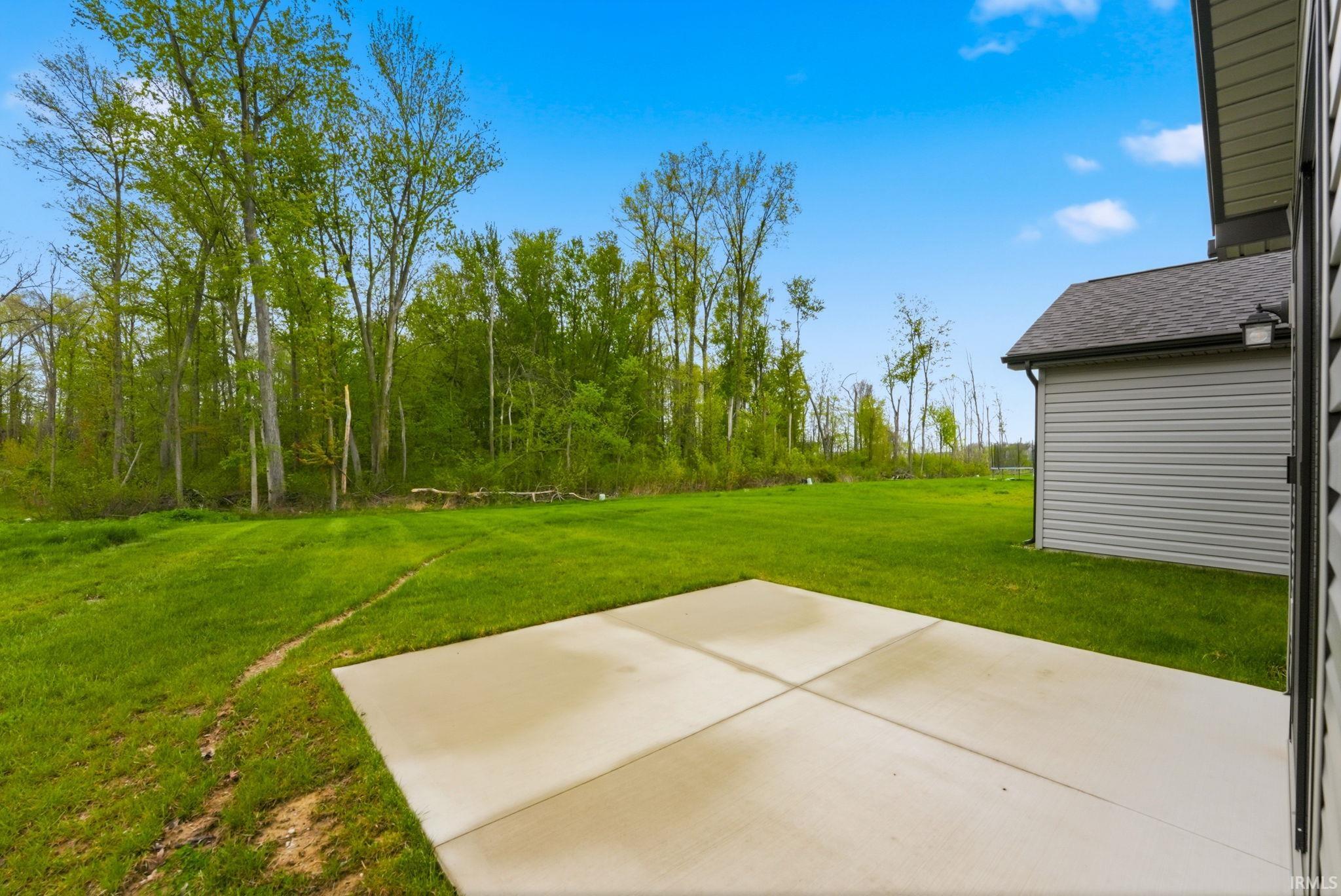 Expansive outdoor space featuring a concrete patio, a lush green lawn, and mature trees bordering the property
