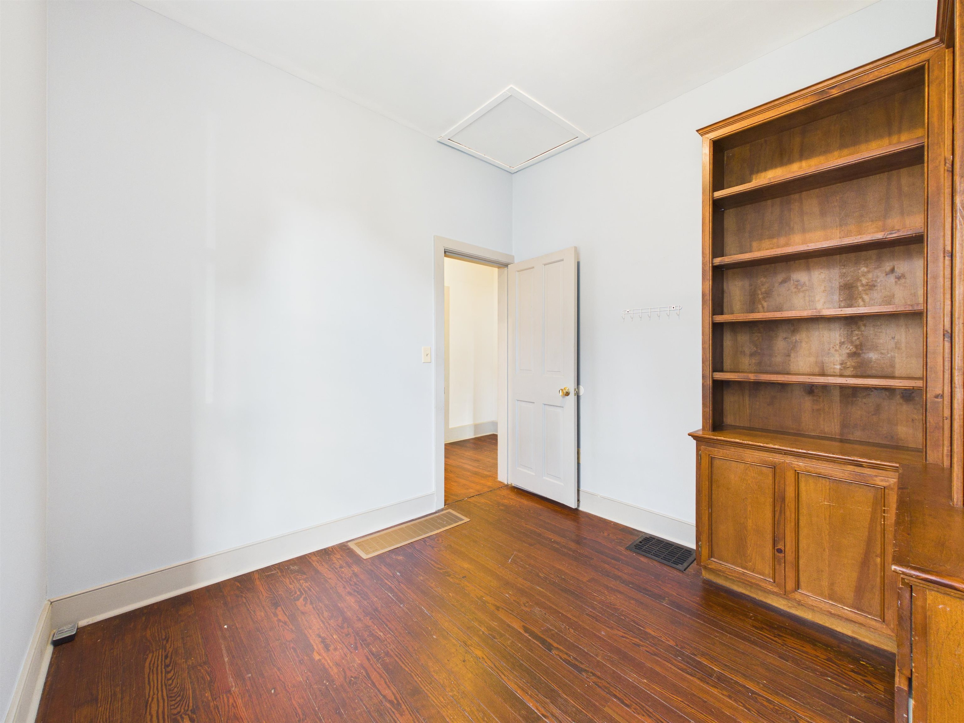 Room featuring wood-finish flooring, white walls, and a built-in wooden bookcase with cabinet storage