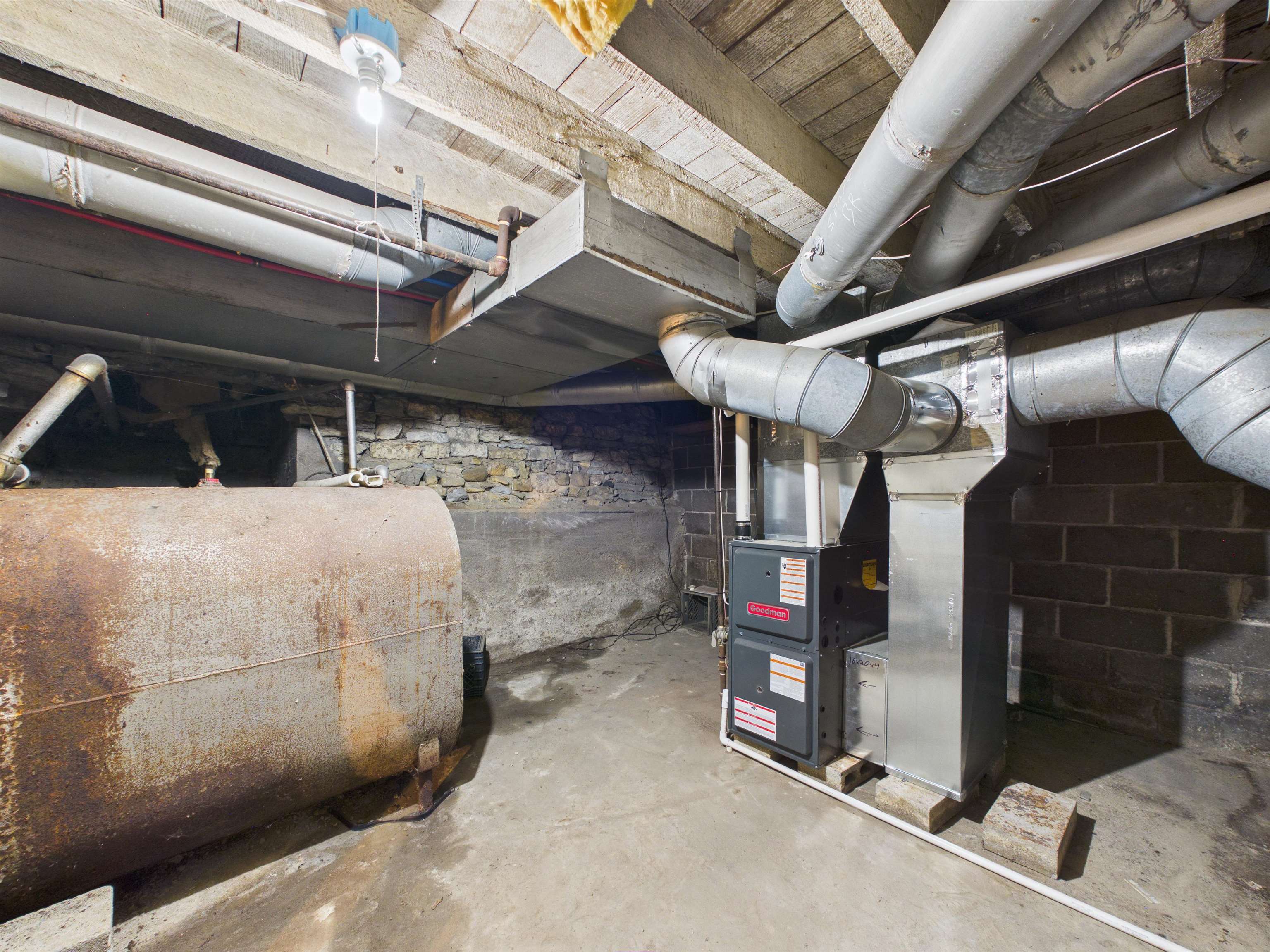 Utility area featuring a modern furnace unit, exposed ductwork, concrete flooring, stone foundation wall, and a fuel oil tank