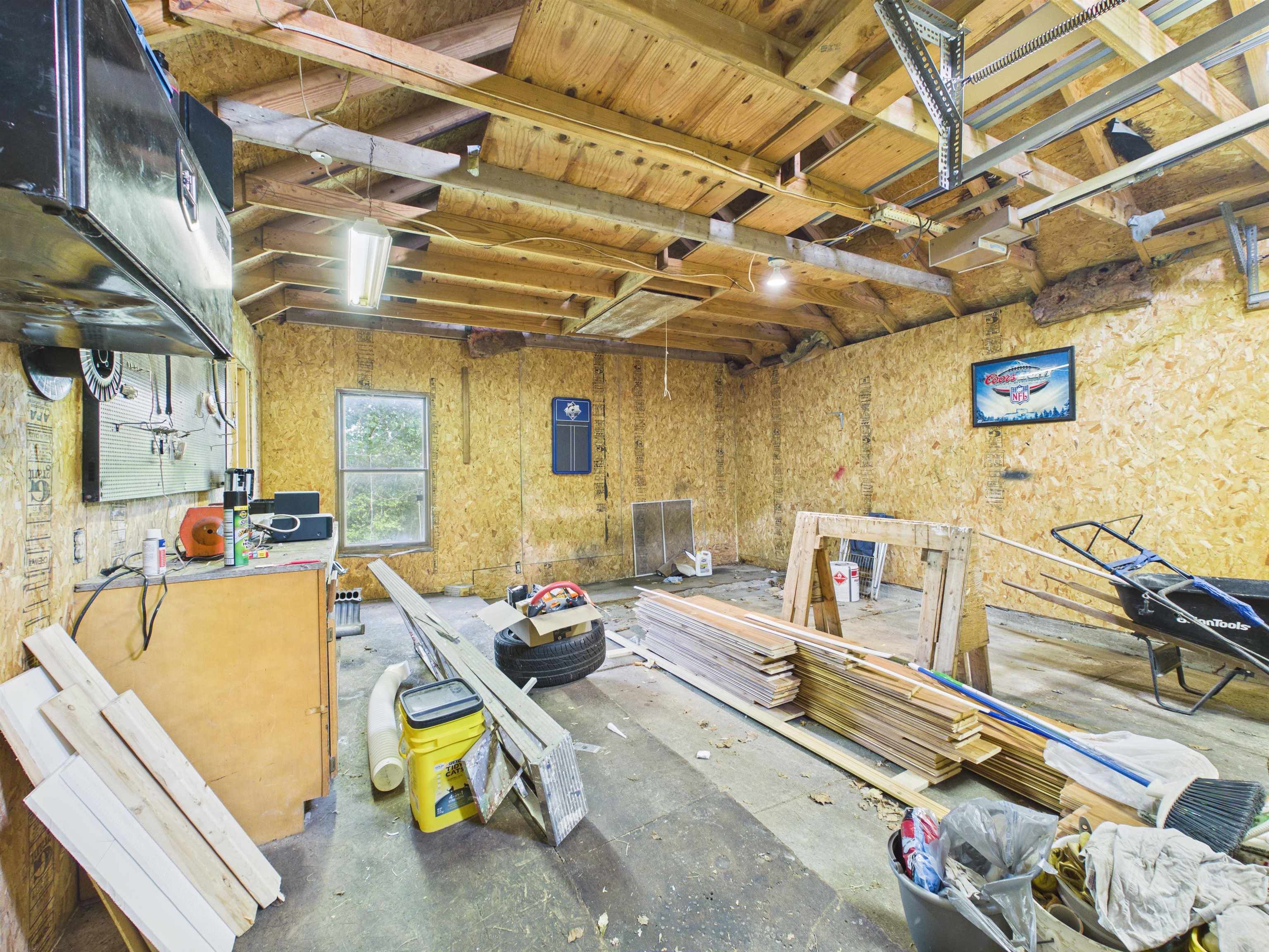 Spacious garage featuring exposed wood framing, oriented strand board walls, and concrete flooring