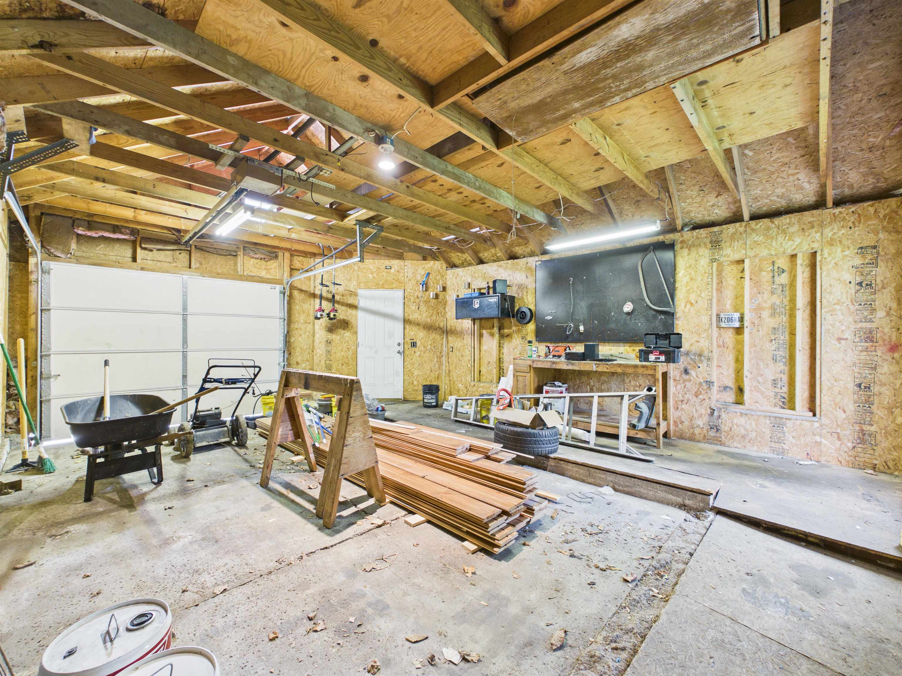 Garage space featuring wood-paneled walls, exposed ceiling beams, and concrete flooring