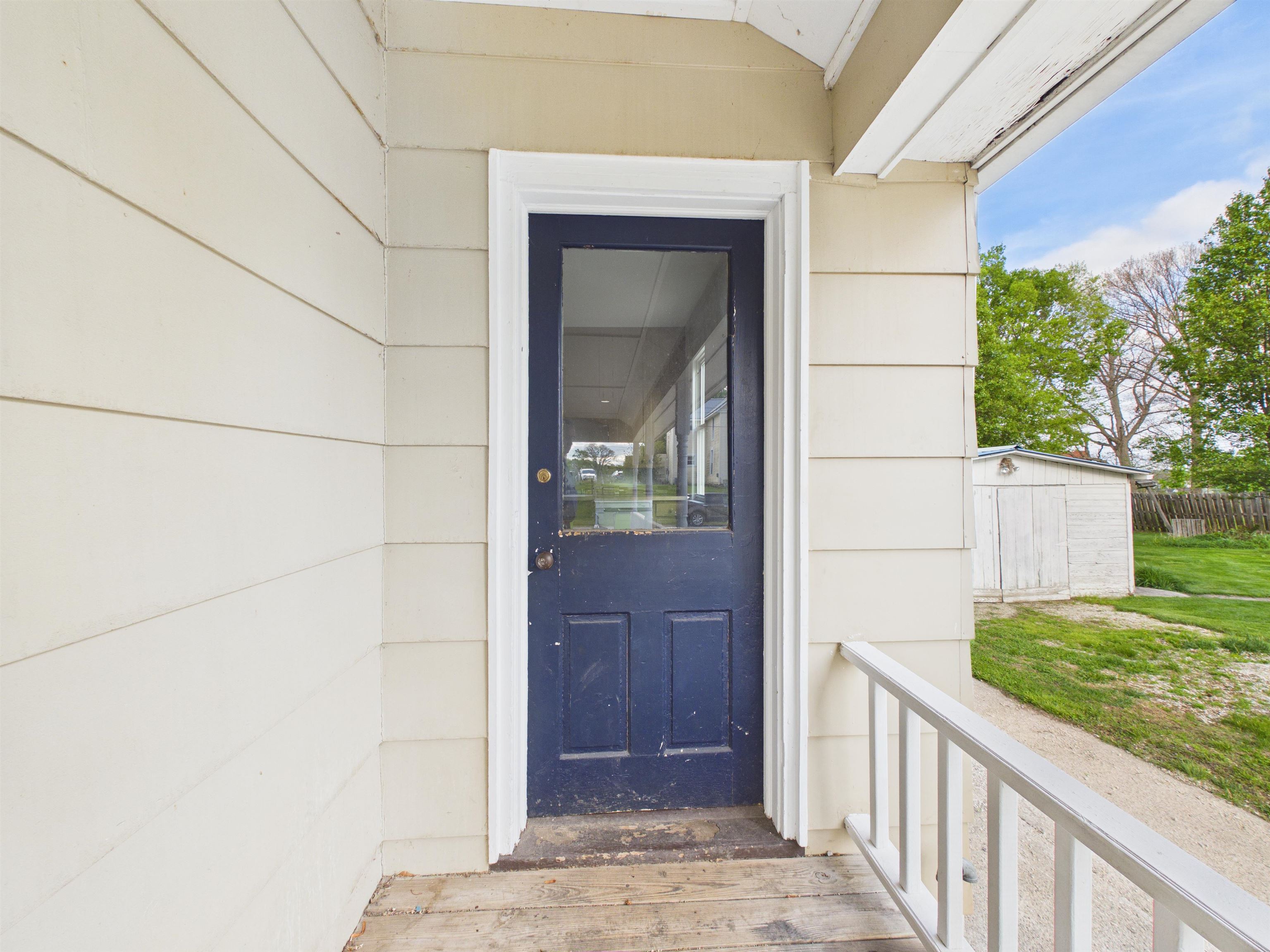 Front porch featuring a paneled door with upper glass insert, wood siding, and painted railing