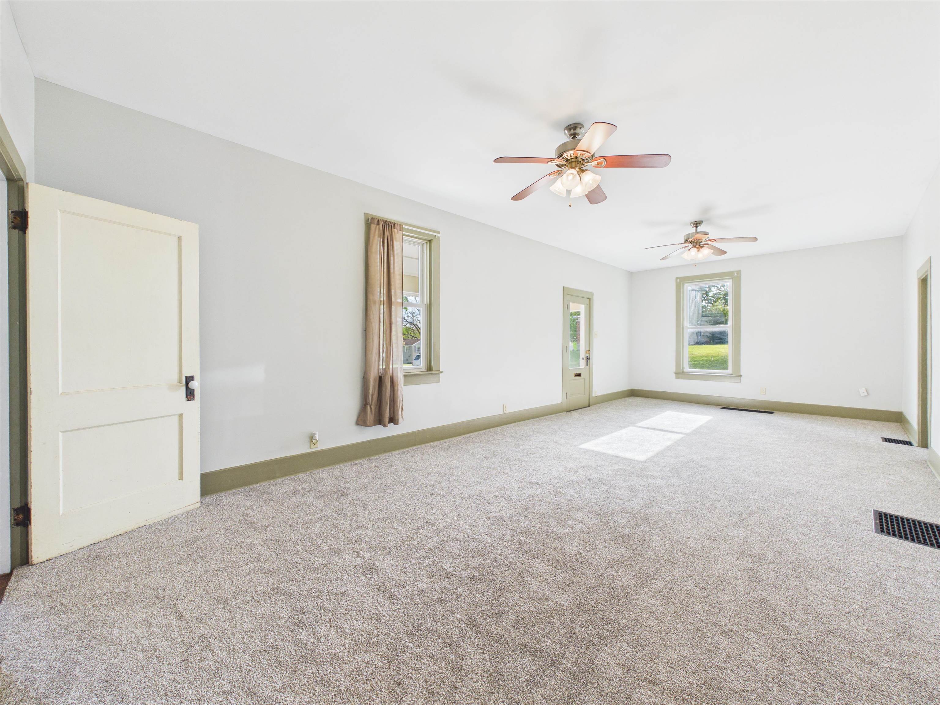 Spacious room featuring light-colored carpeting and white walls with green trim