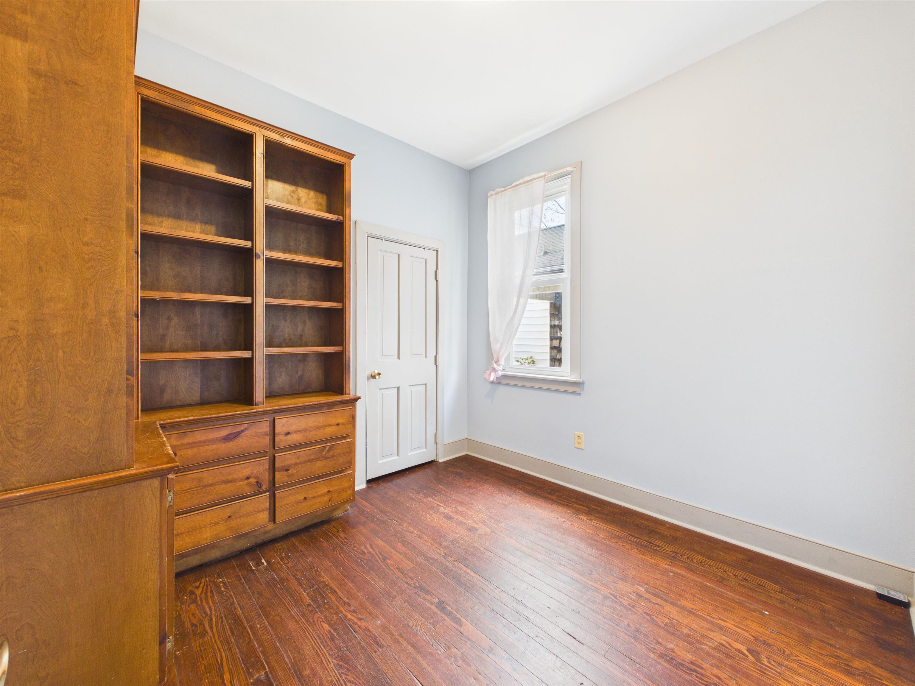 Room featuring wood-finish flooring, built-in shelving, built-in drawers, a single window, and a paneled door