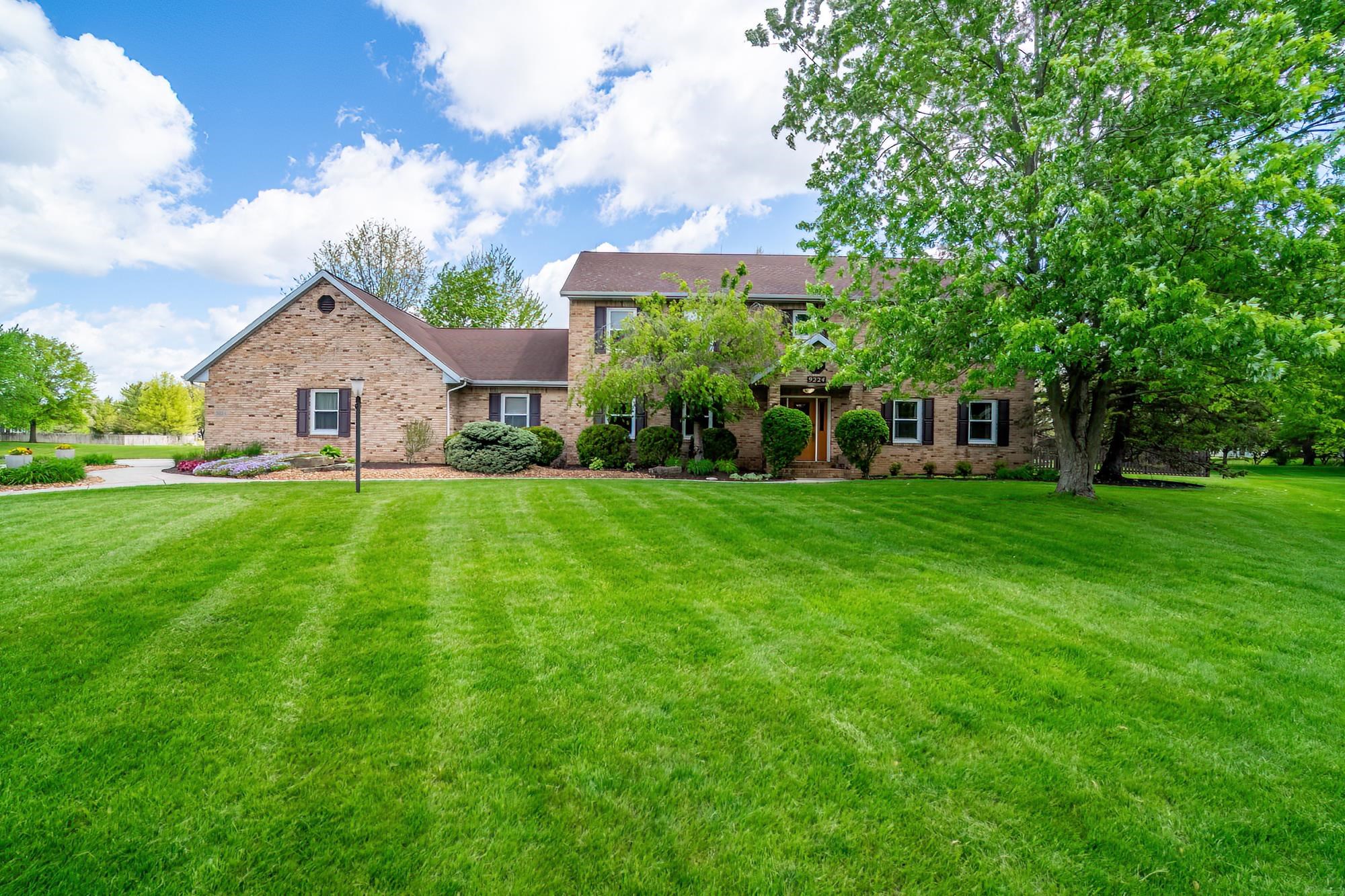 Brick exterior home featuring dark shutters, a prominent gable, and mature front yard landscaping