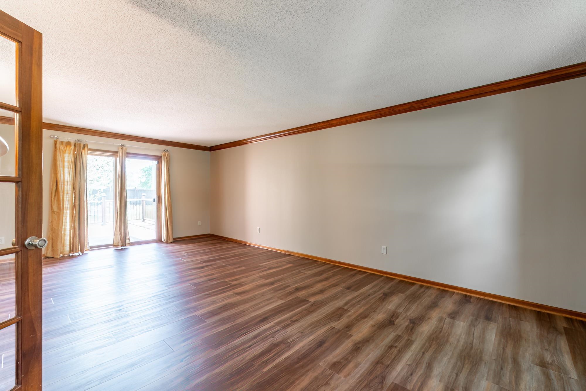 Spacious room featuring wood-finish flooring, light neutral wall paint, and wood trim