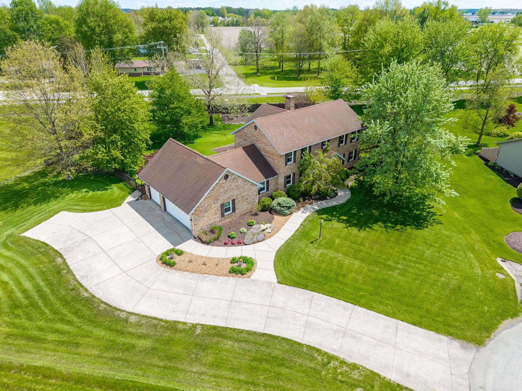 Two-story brick residence with an attached two-car garage, featuring a large concrete driveway and mature landscaping