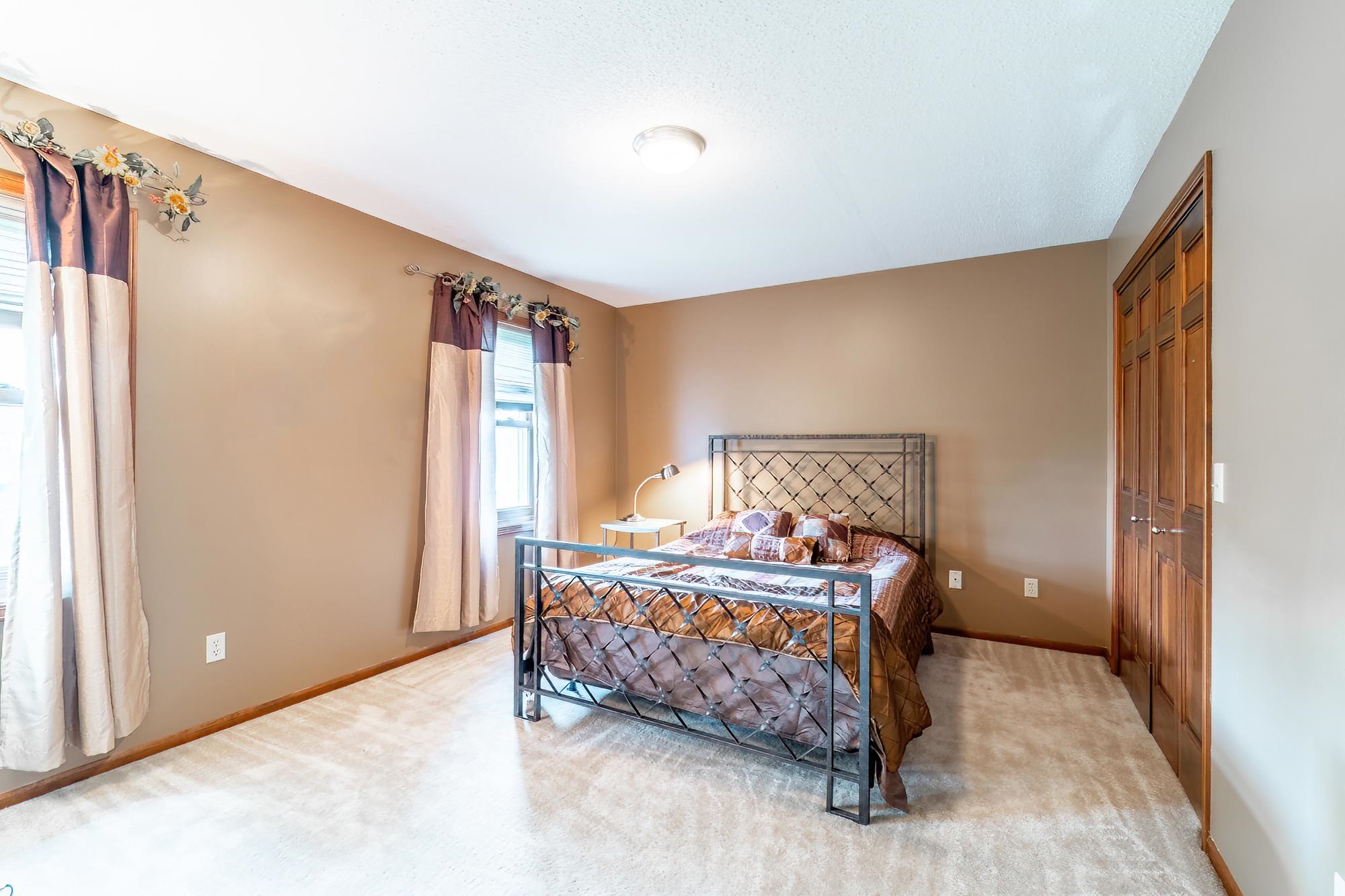 Carpeted room featuring a ceiling-mounted light fixture, two windows with blinds, and a built-in bifold closet with wood-finish doors
