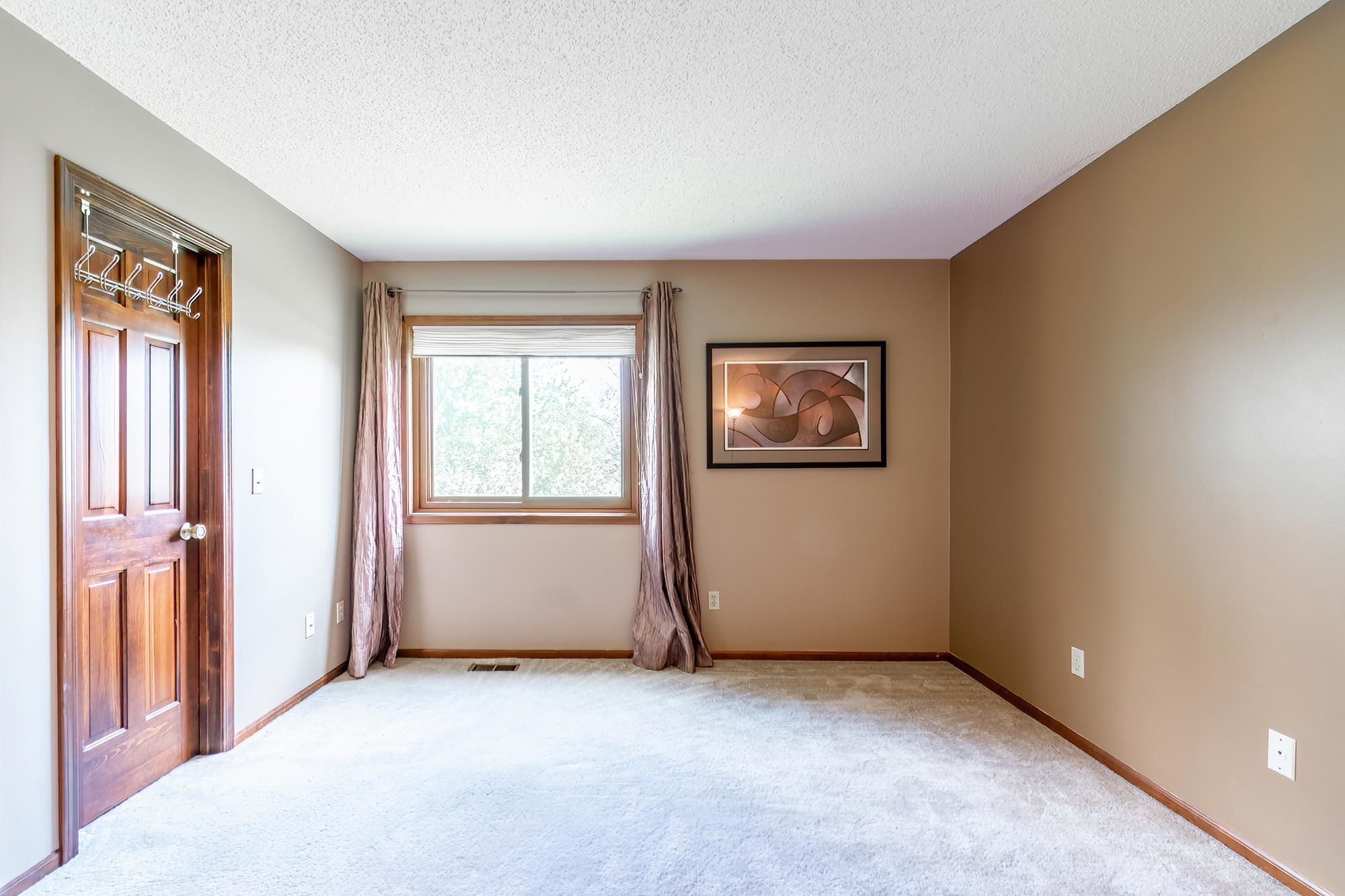 Bright interior space featuring a paneled wood door, light-colored carpeting, a window with wood trim, and neutral wall paint