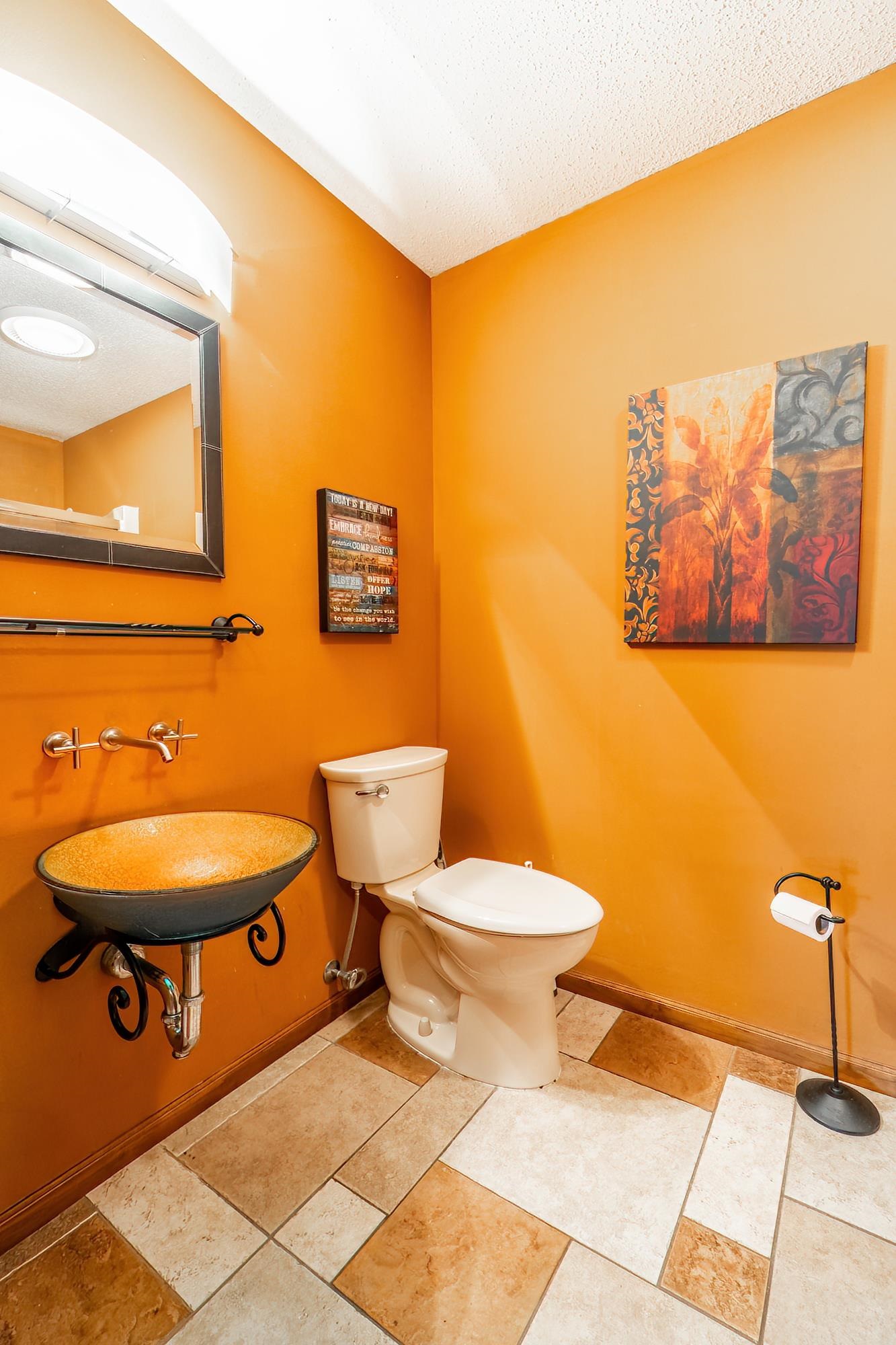Powder room featuring a decorative vessel sink with wall-mounted brass fixtures, a toilet, and patterned tile flooring