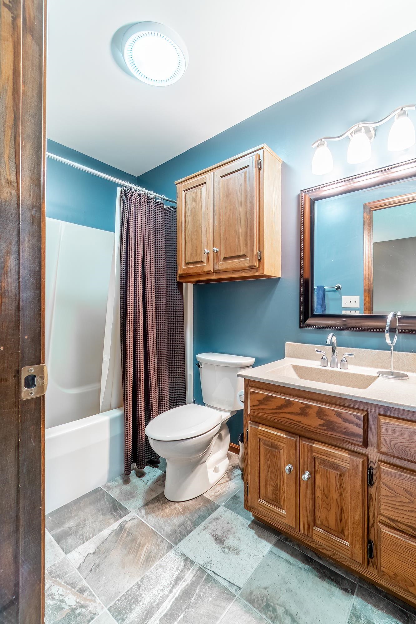 Bathroom featuring a wood vanity with a light-toned countertop, a framed mirror, a tub/shower combination, and tiled flooring