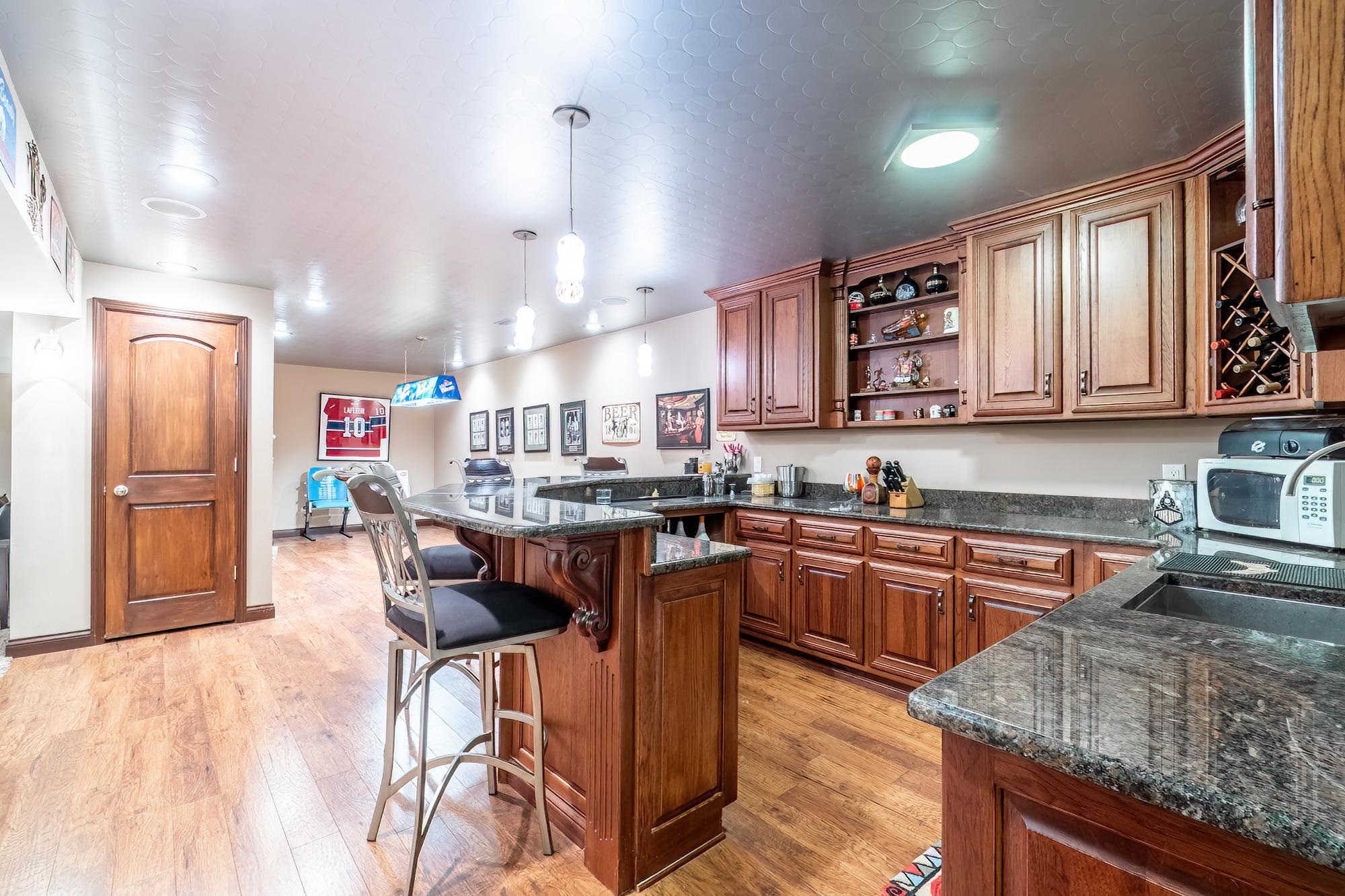 Wood-finish flooring throughout a spacious room featuring a built-in bar with granite-style countertops, wood cabinetry, and recessed lighting