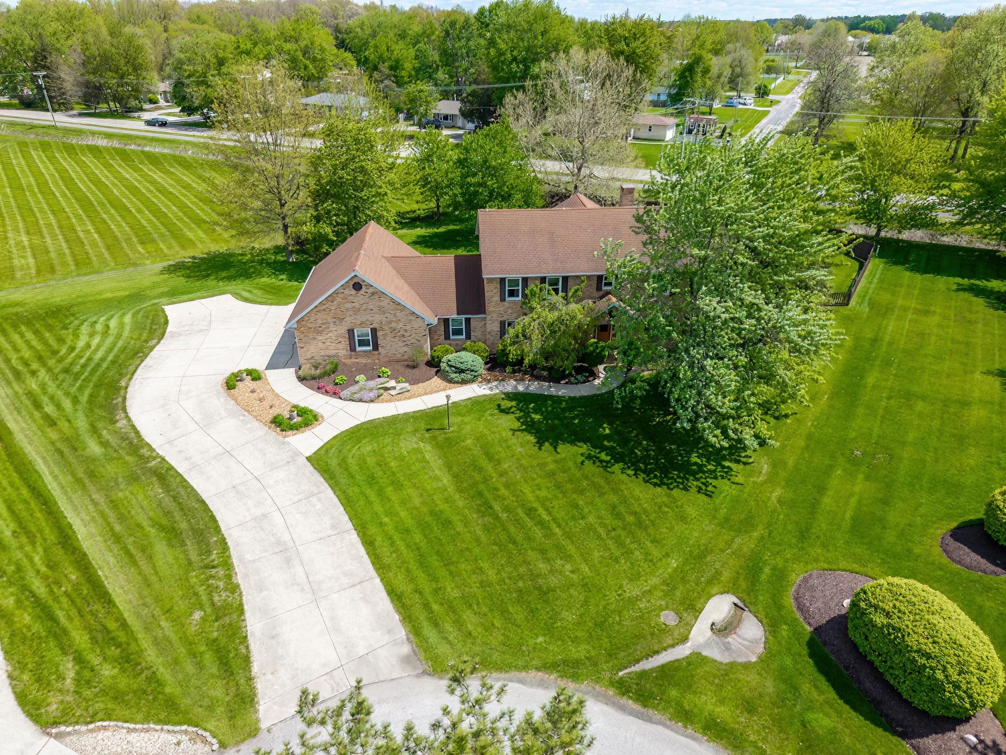 Expansive property featuring a brick exterior residence with a multi-gabled roofline, a winding concrete driveway, mature trees, and extensive green space