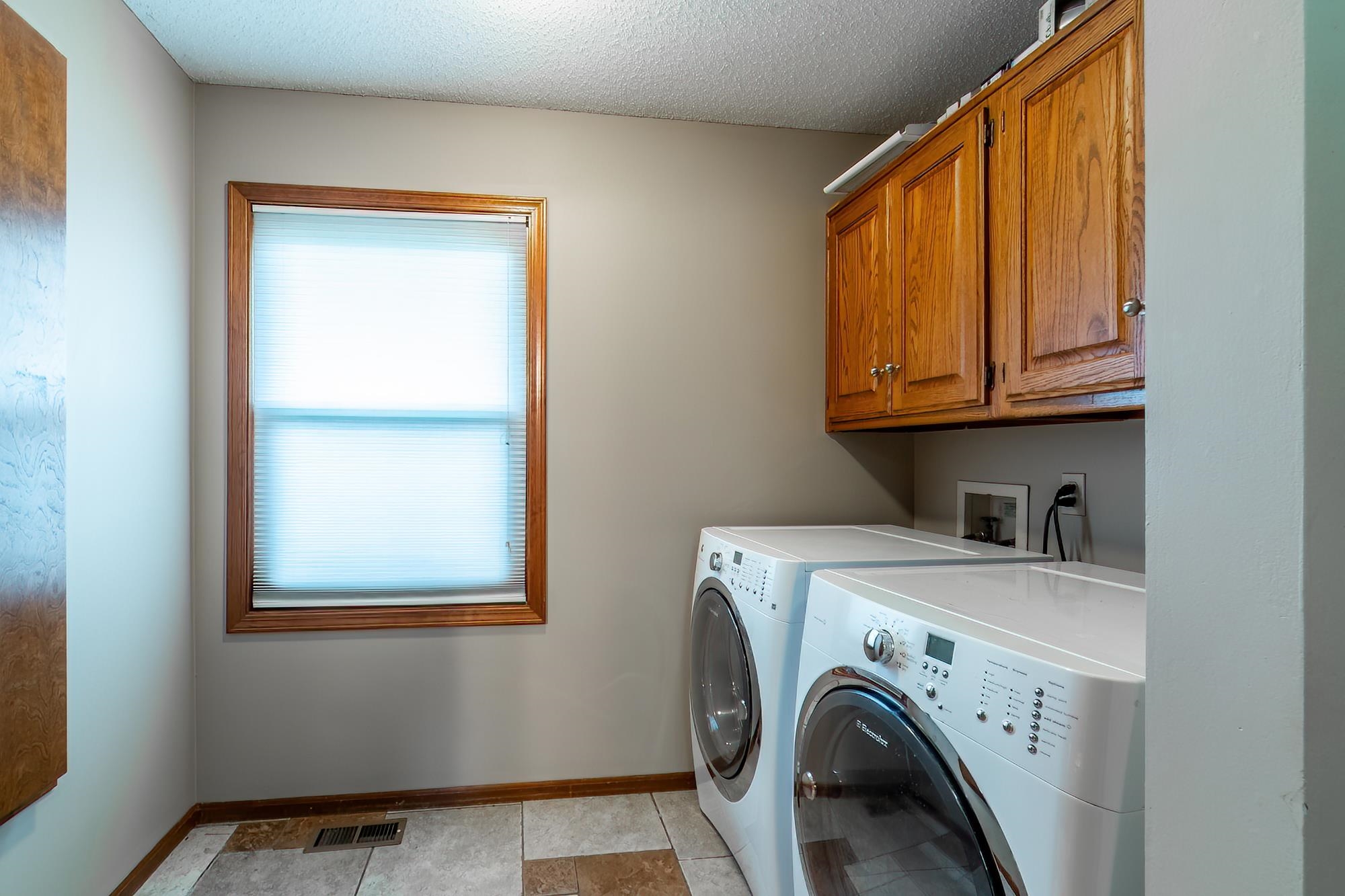 Laundry area featuring wood-finish cabinetry, a window with wood trim, and tiled flooring