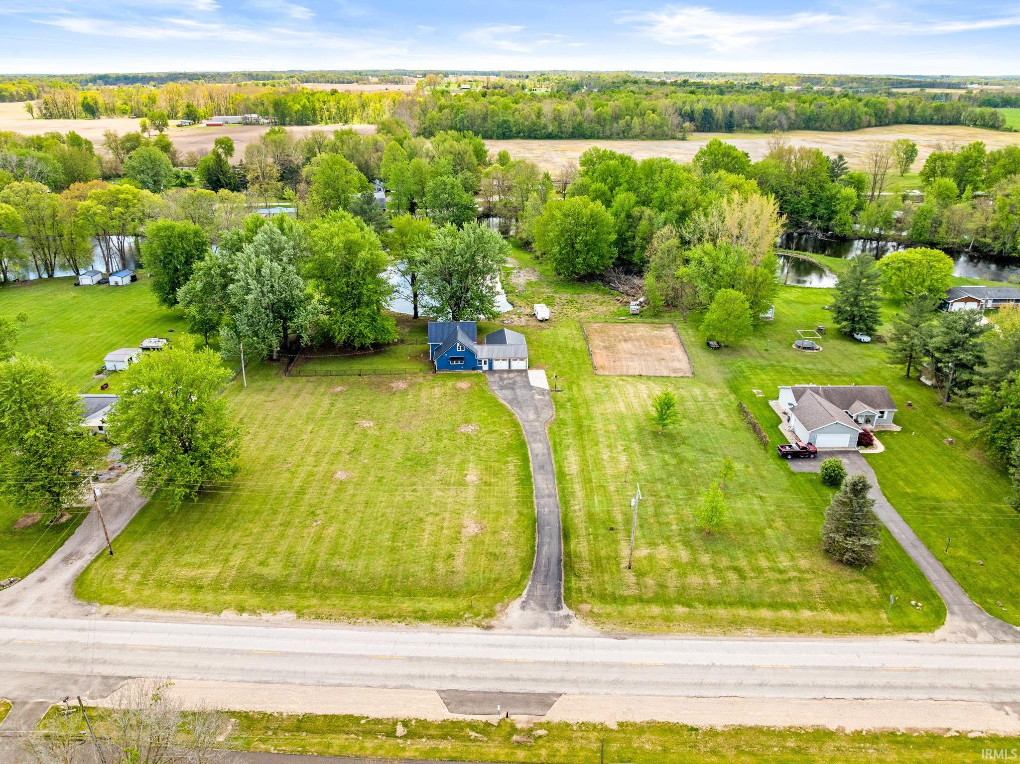 Expansive green acreage featuring a long driveway, surrounding mature trees, and a visible body of water