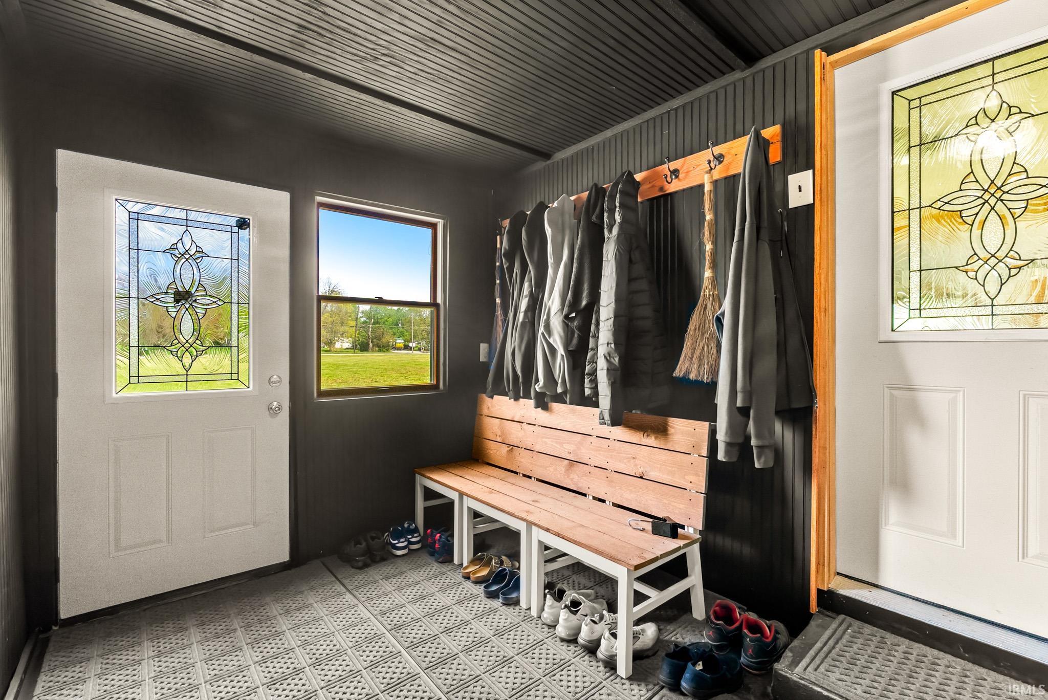 Entryway featuring two white doors with decorative glass inserts, a single-pane window, and a built-in wooden bench with coat hooks